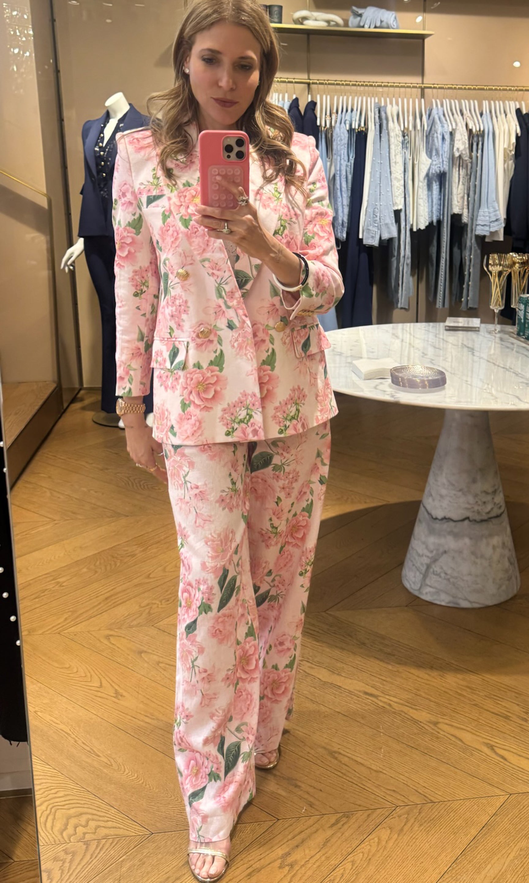 Woman in a floral suit taking a mirror selfie in a clothing store.