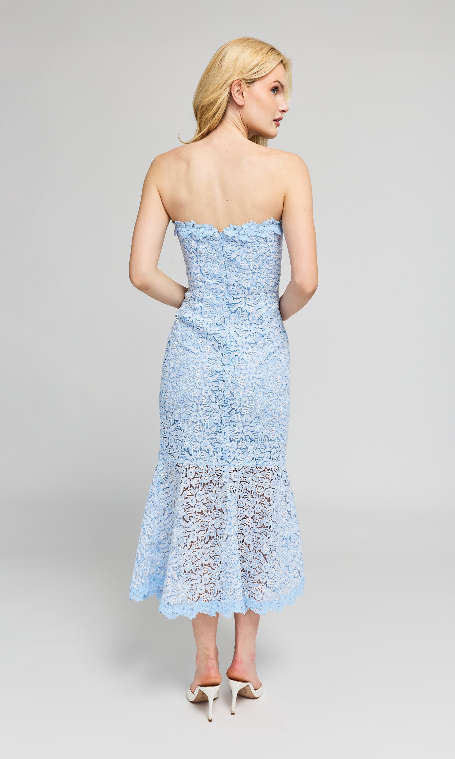 Back view of woman wearing a light blue strapless lace dress and white heels.