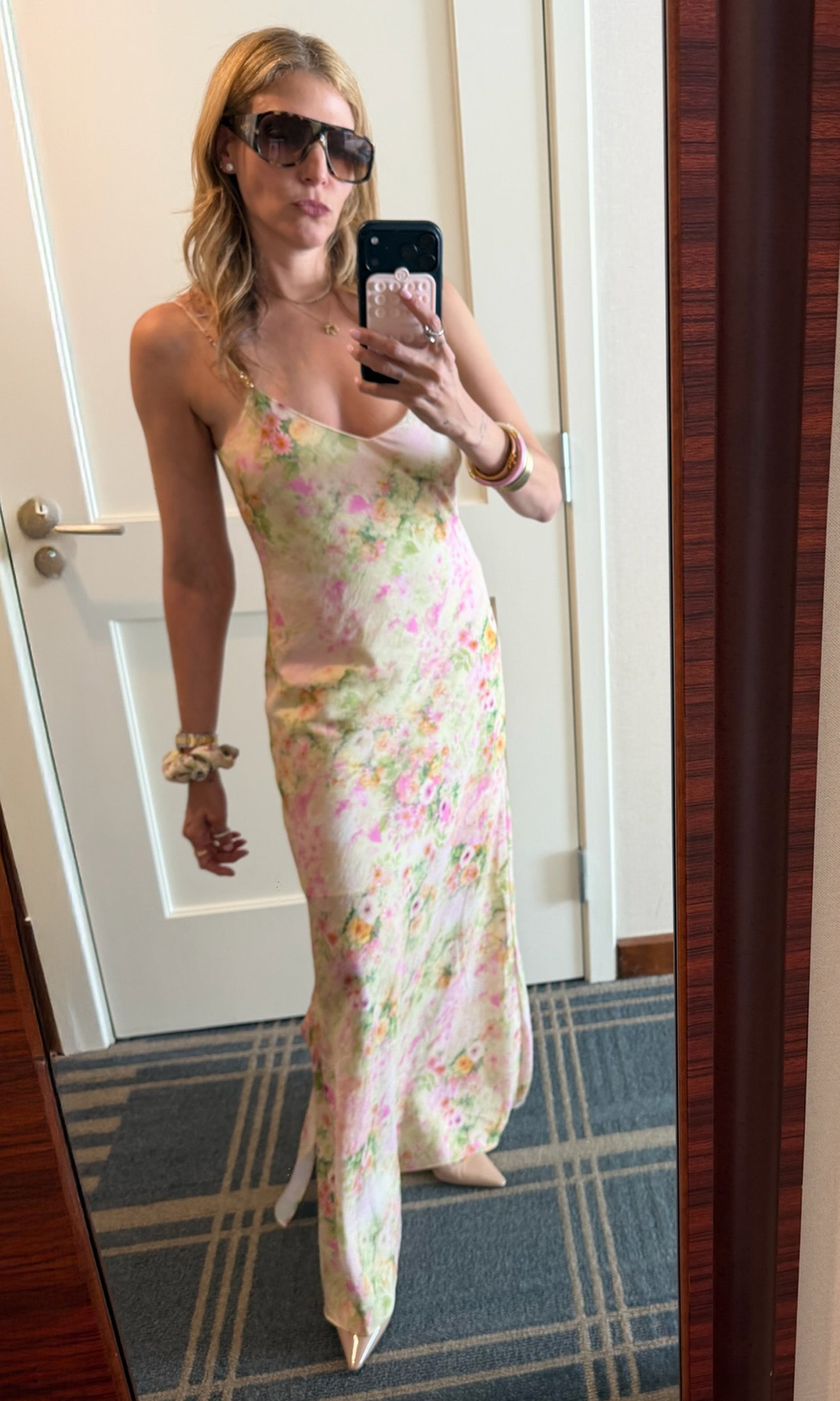 Founder Roni posing in front of a mirror wearing a white floral dress with beige heels.