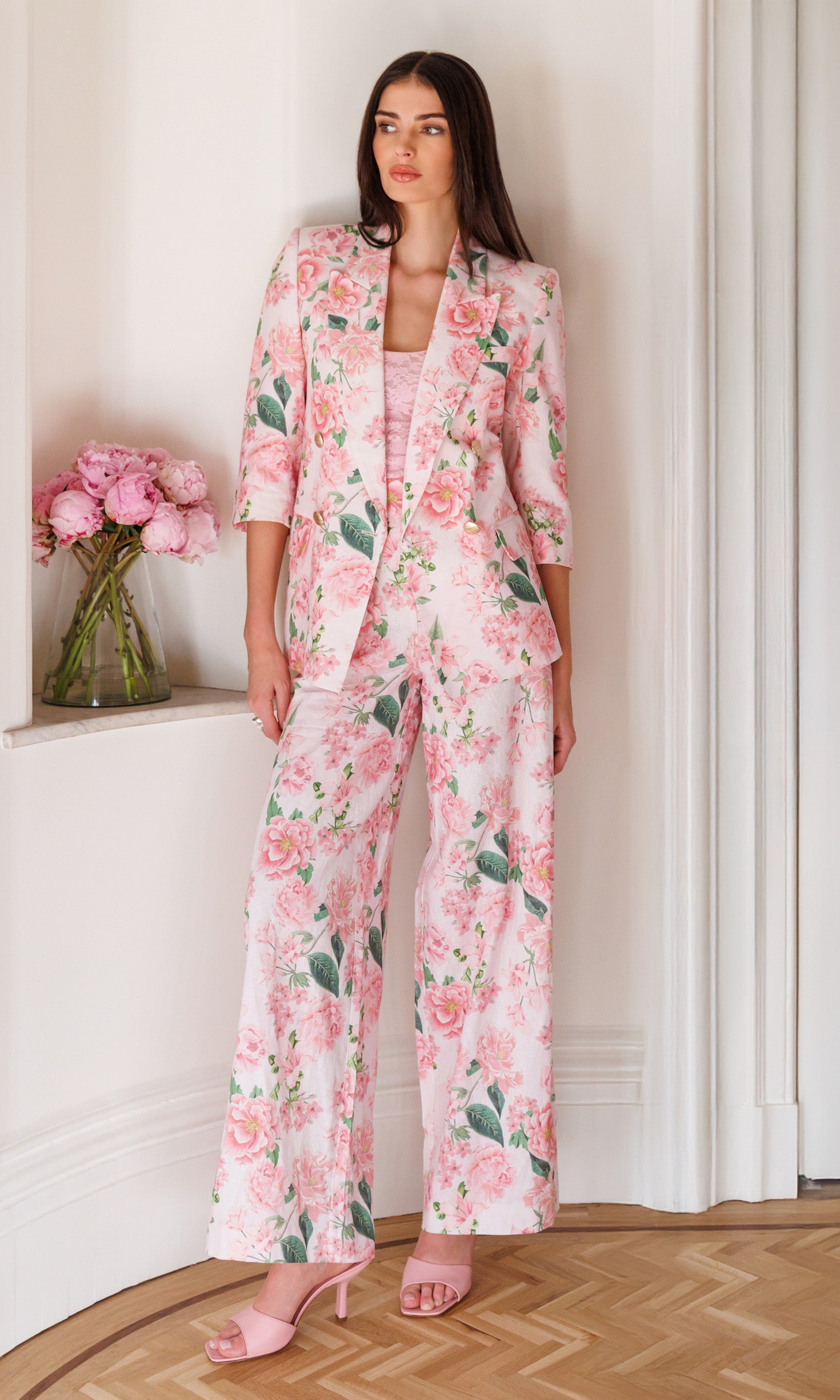 Woman wearing a pink floral suit standing in a room with peony flowers.