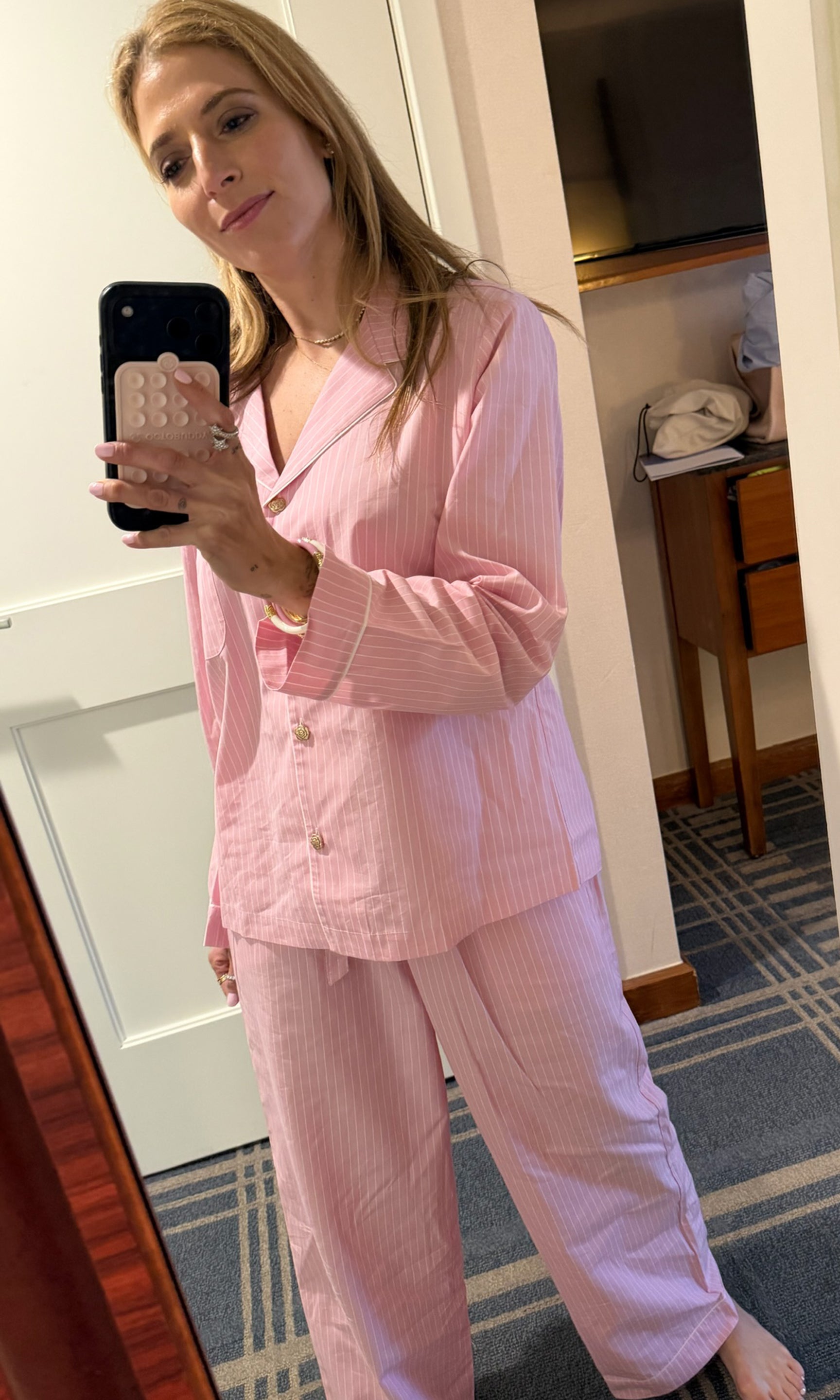 Founder Roni takes a mirror selfie wearing a light pink and white vertically striped pajama set.