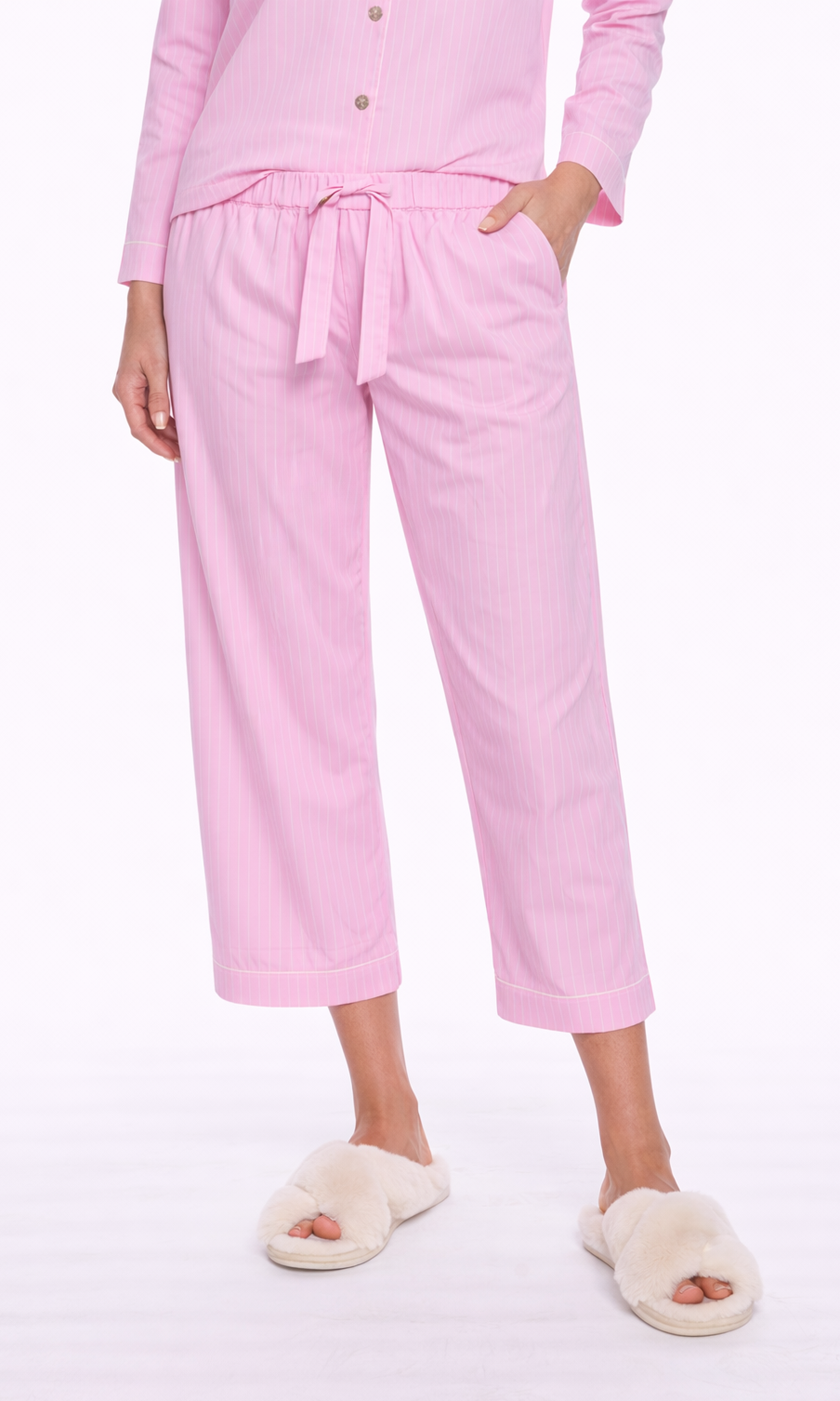 Person wearing pink pajama set with white slippers on a white background