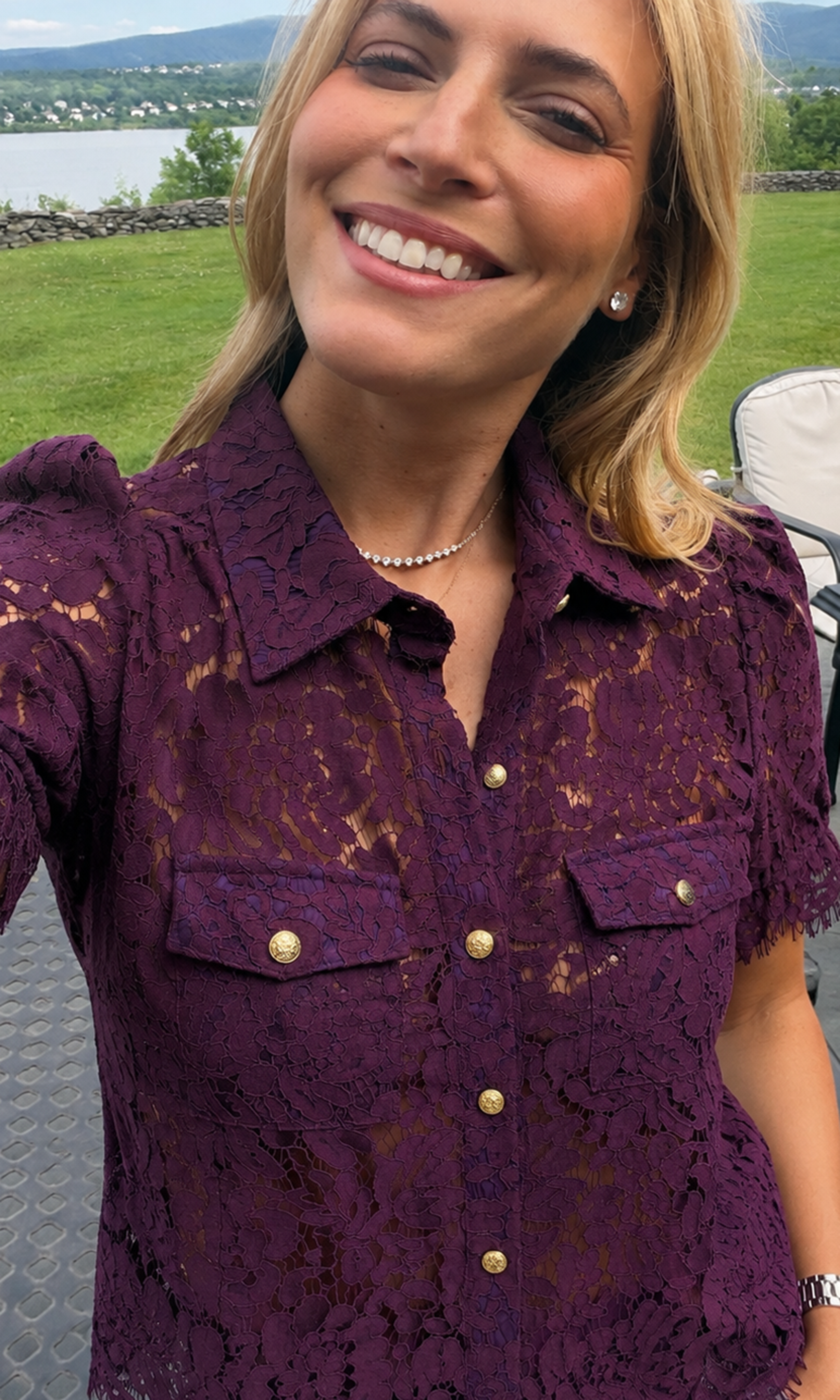 A woman wearing a short-sleeve purple lace button-up shirt with gold buttons, photographed outdoors.