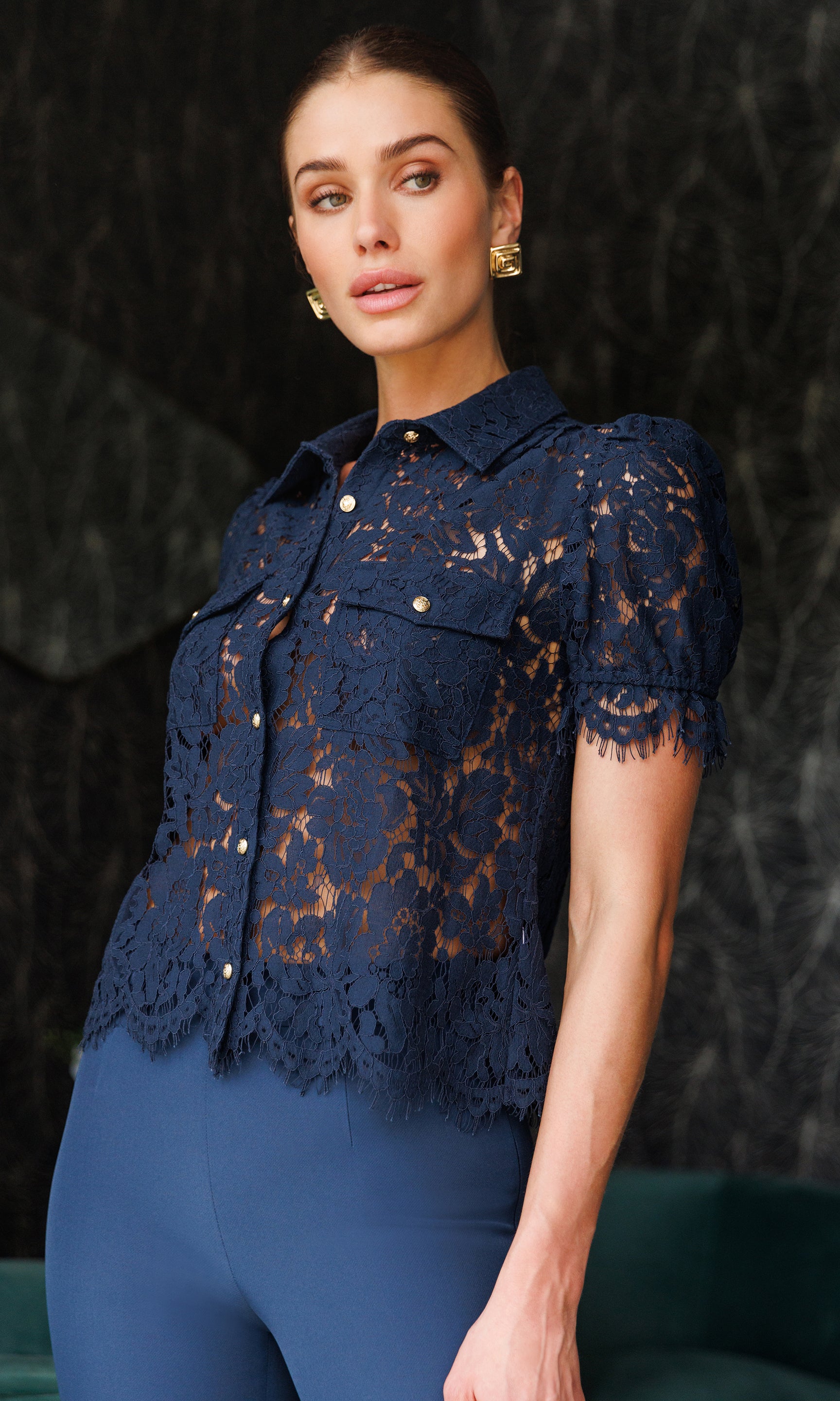 Woman wearing a navy lace top against a dark background