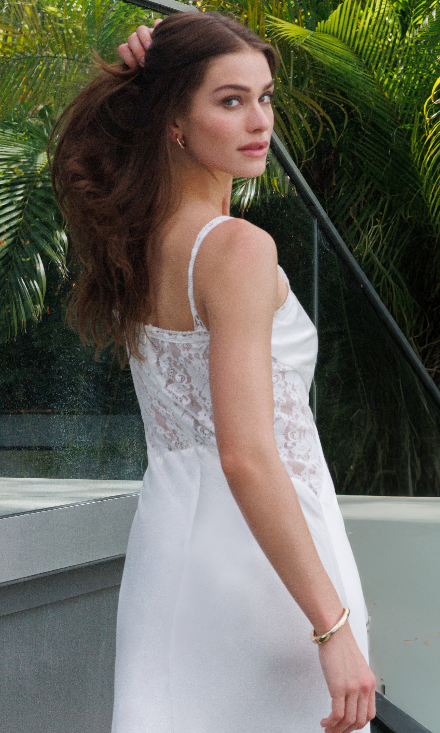 Woman in a white dress standing outdoors with greenery in the background