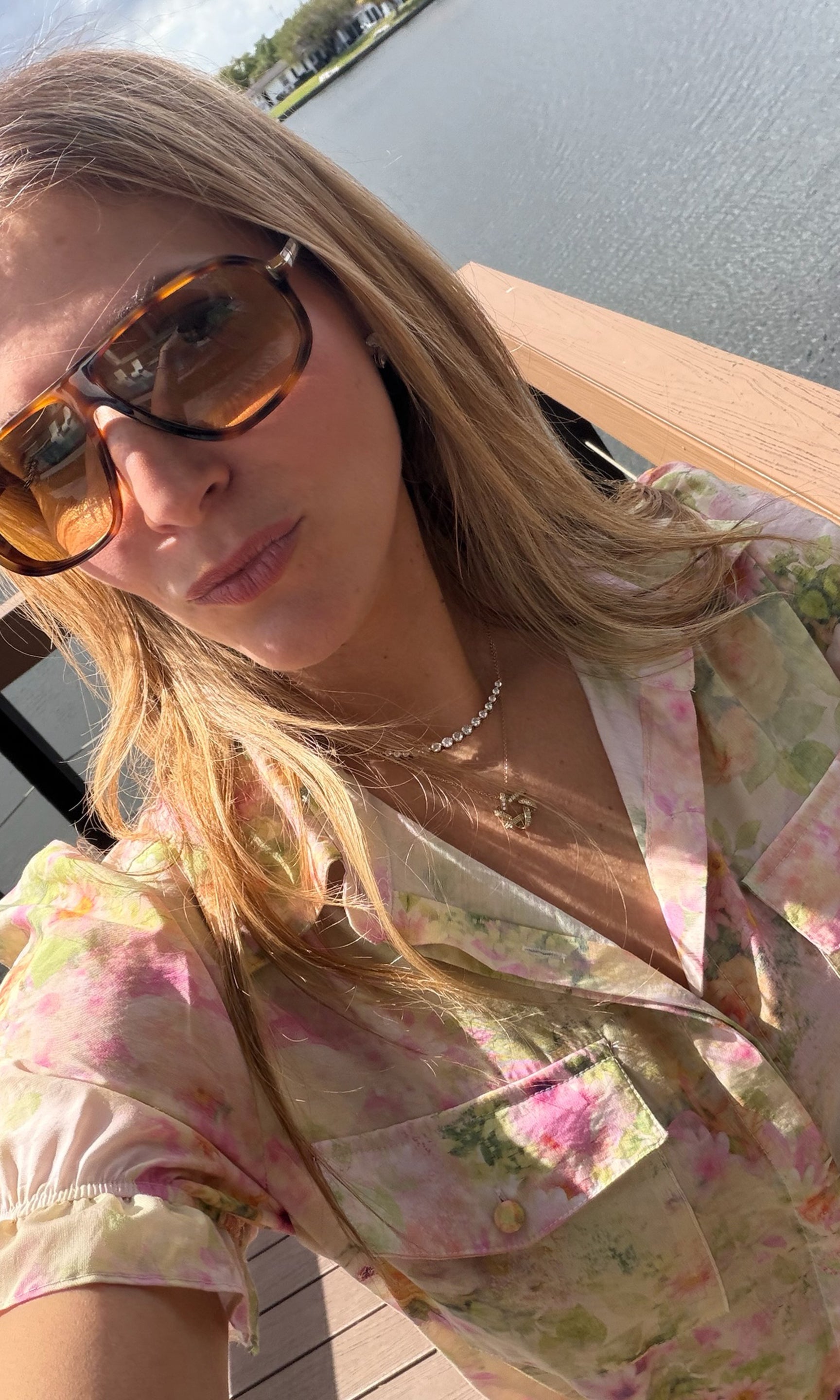 Woman wearing sunglasses and a floral top by a body of water