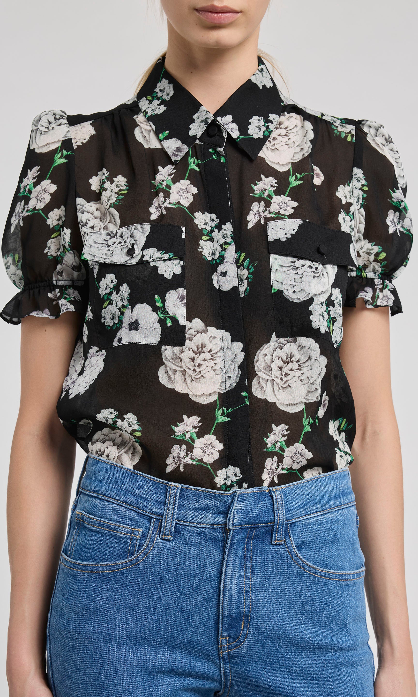 Black floral blouse with white flowers worn by a person on a white background