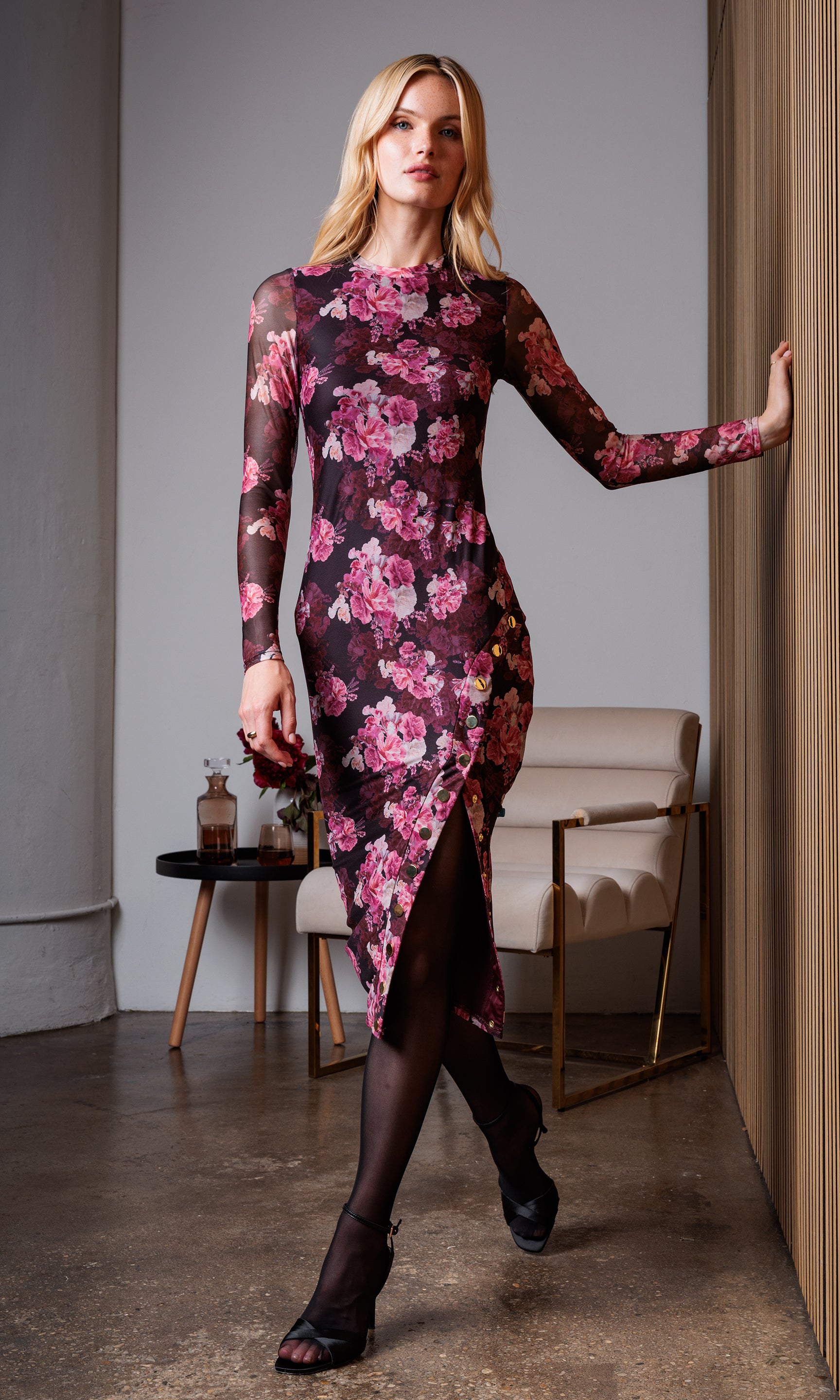 Woman wearing the Monique floral dress in an indoor setting with a beige chair and black table in the background