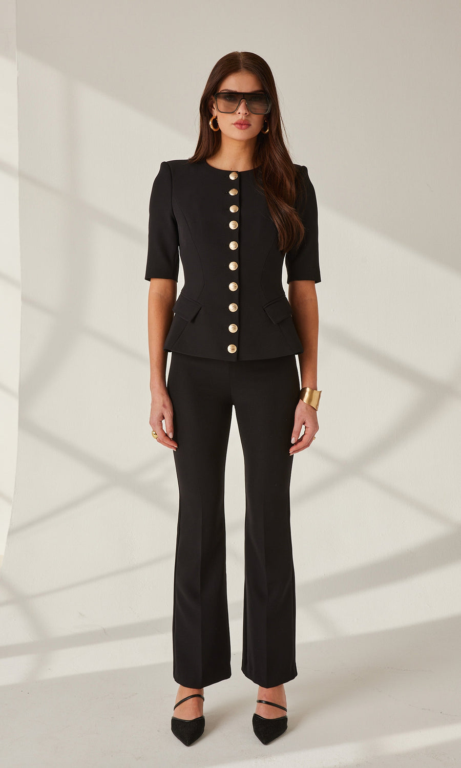 A model showcases a black blazer with gold buttons and matching crepe pants, exuding elegance and style.