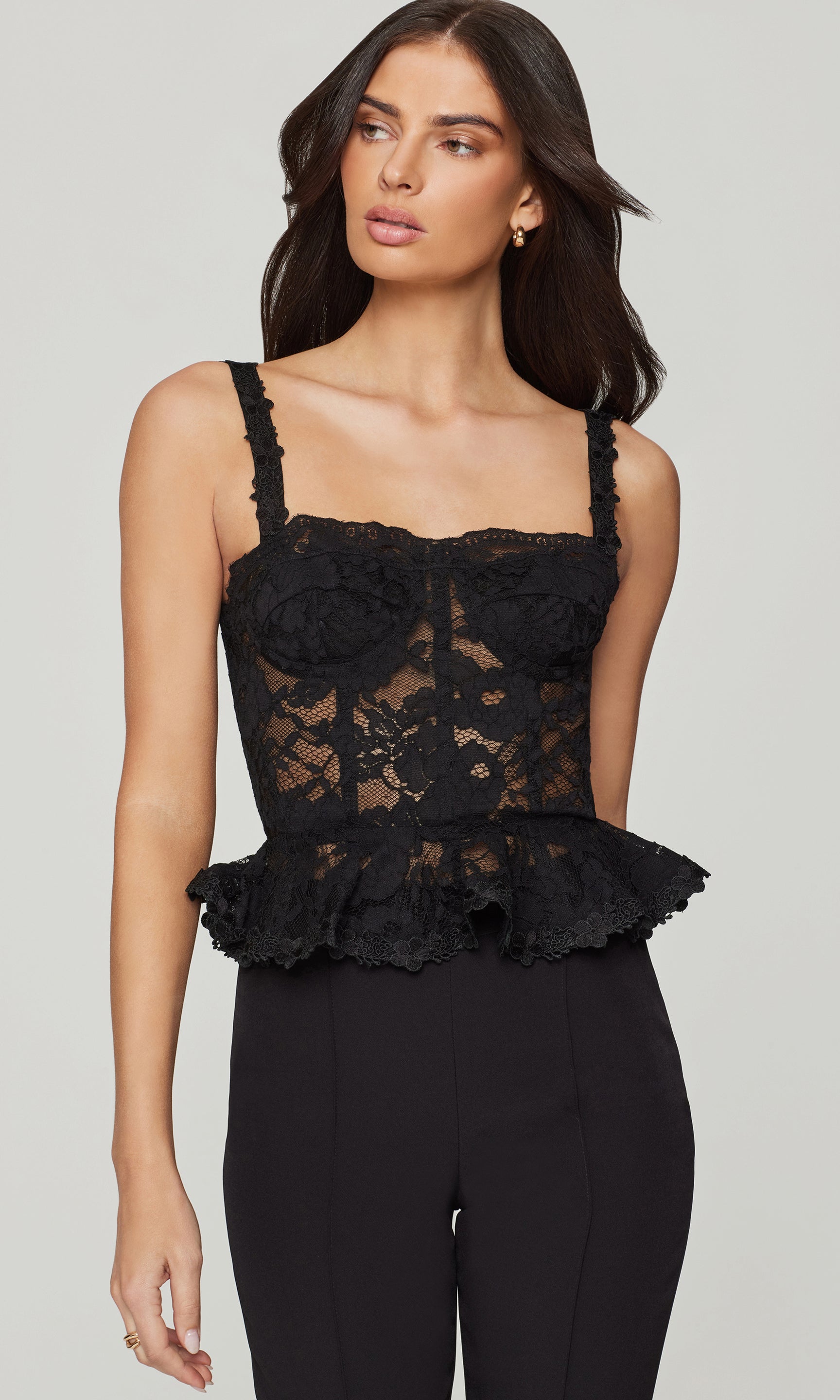 Woman wearing a black lace top with ruffled details on a plain background