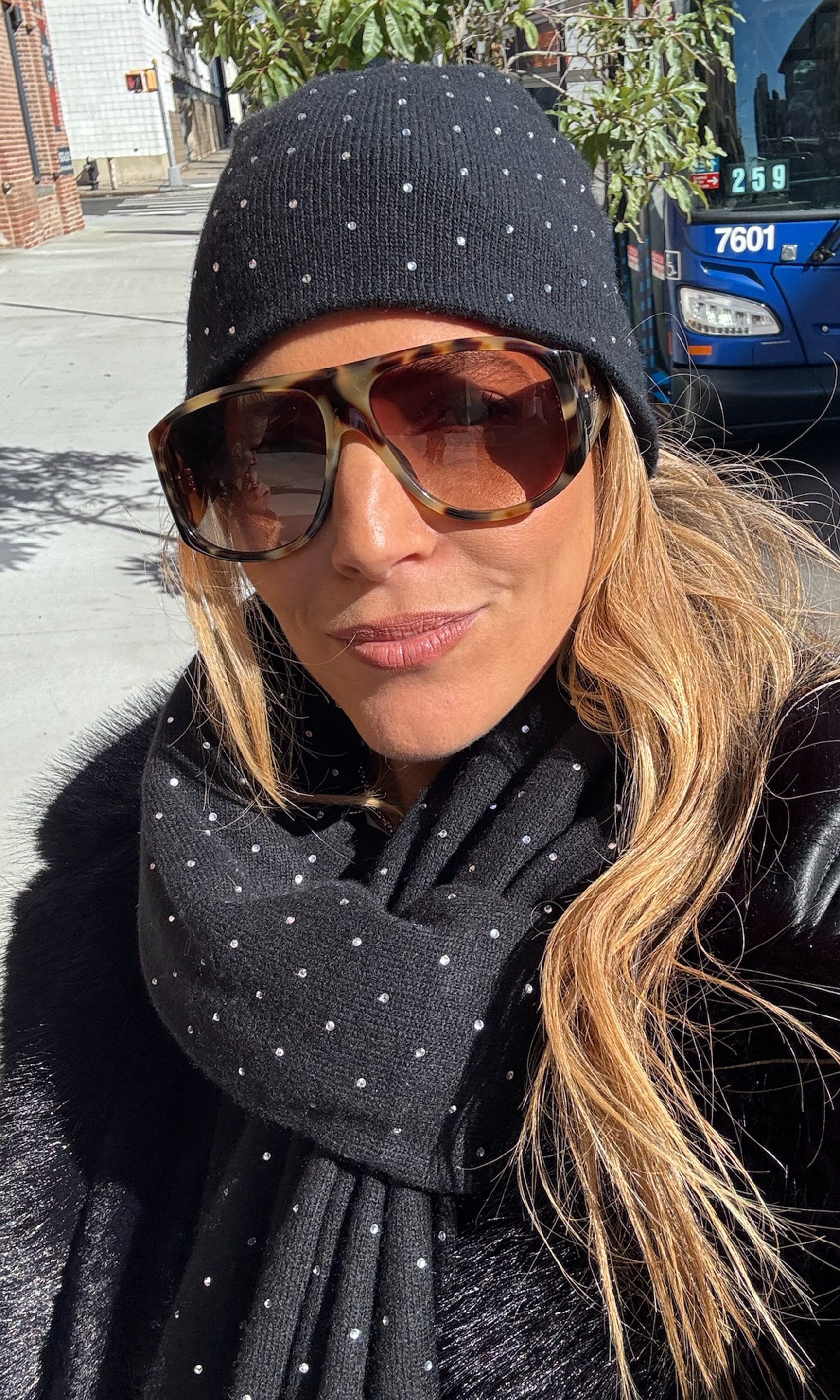 Person wearing a black polka dot beanie and scarf on a street with a bus in the background.