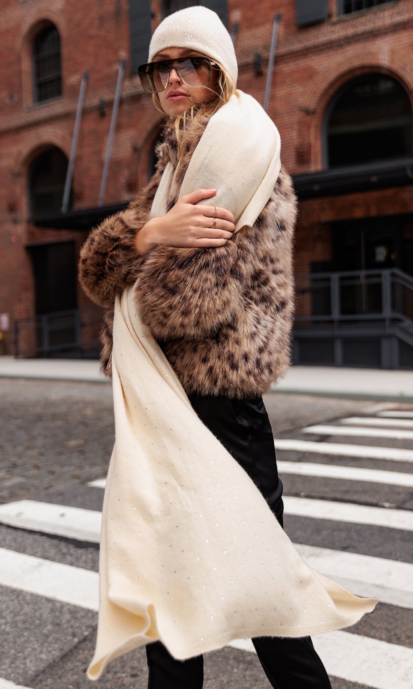 Woman wearing a leopard print coat, white hat, and scarf on a city street.