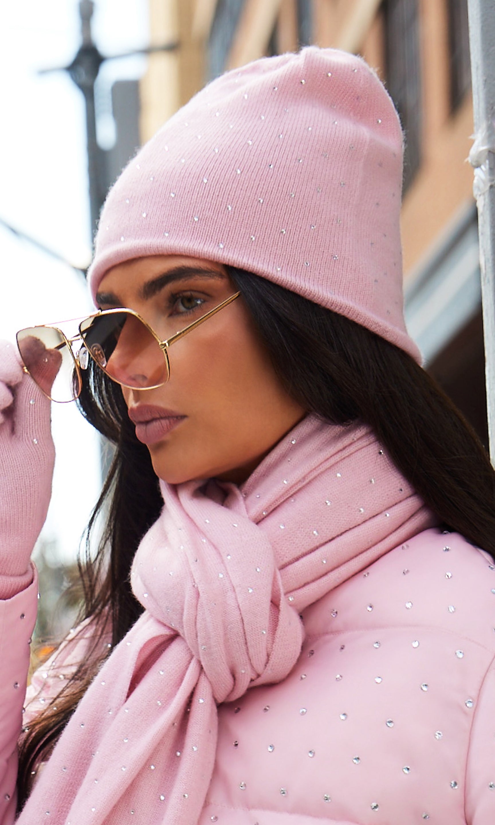 Woman wearing a pink outfit with a coat, scarf, and beanie outdoors.