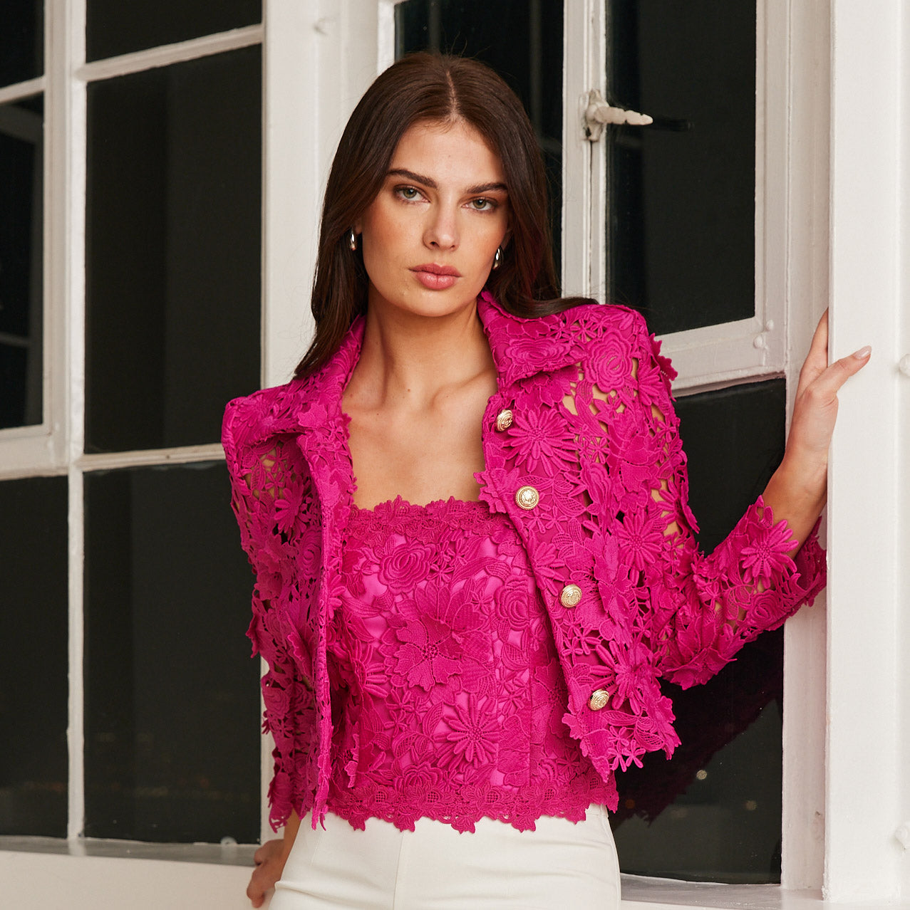 woman stands near window wearing a hibiscus pink floral lace jacket with matching bustier