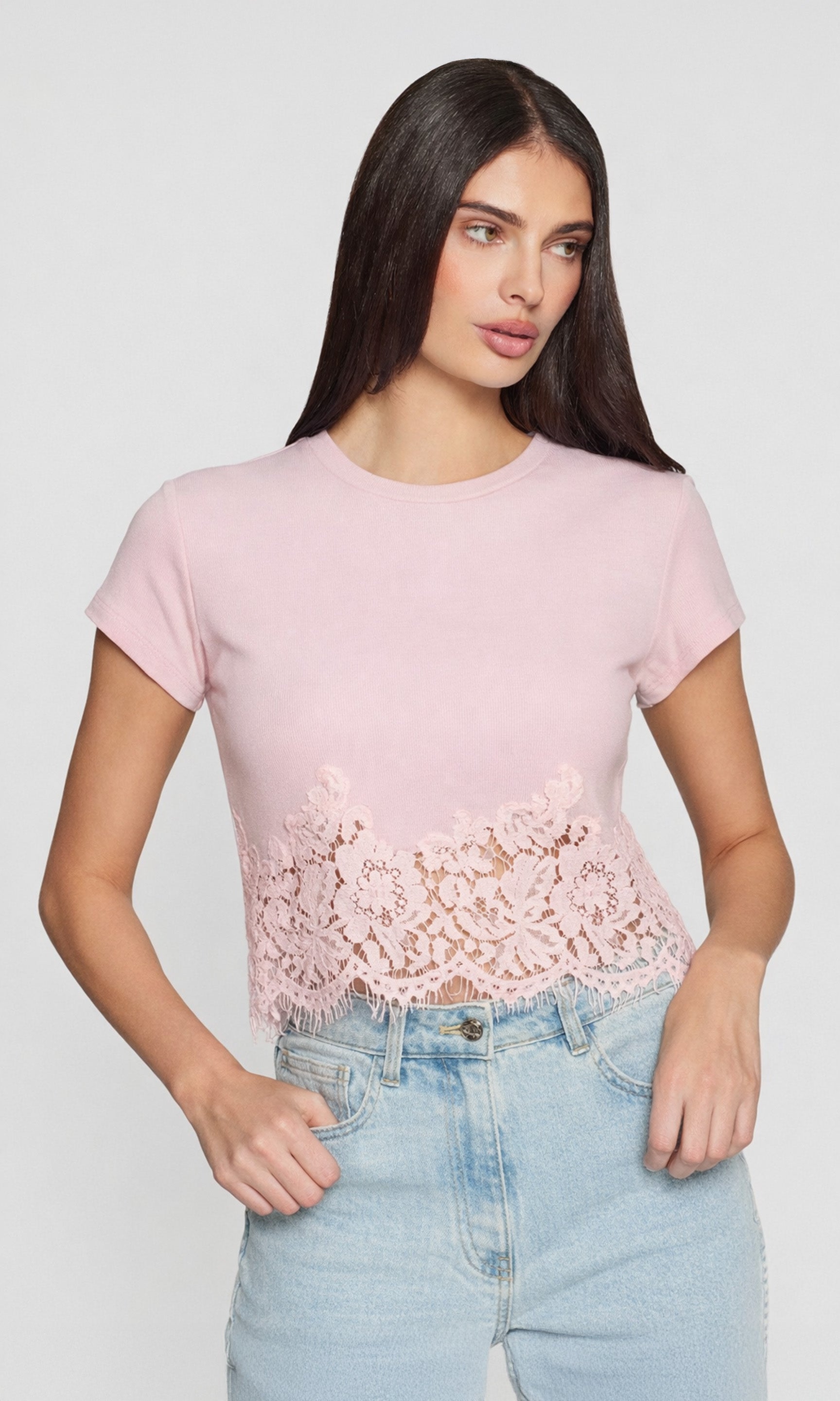 Model wearing a pink top with a lace detailed hem with blue jeans