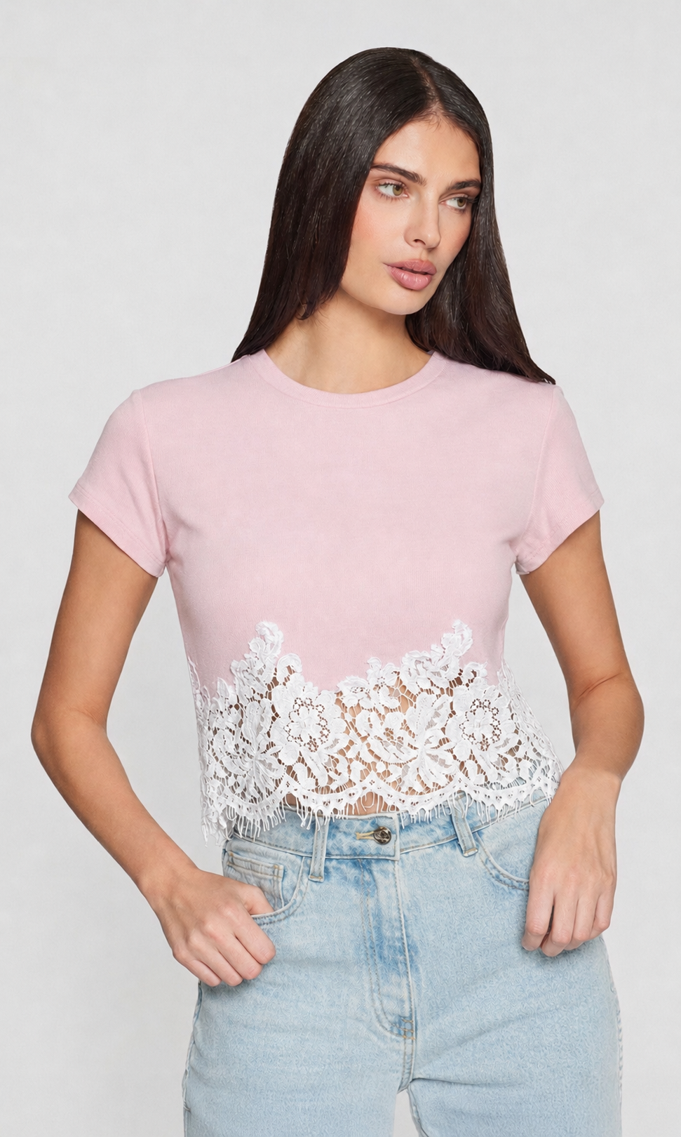 Woman wearing a pink t-shirt with lace detailing and light blue jeans on a white background