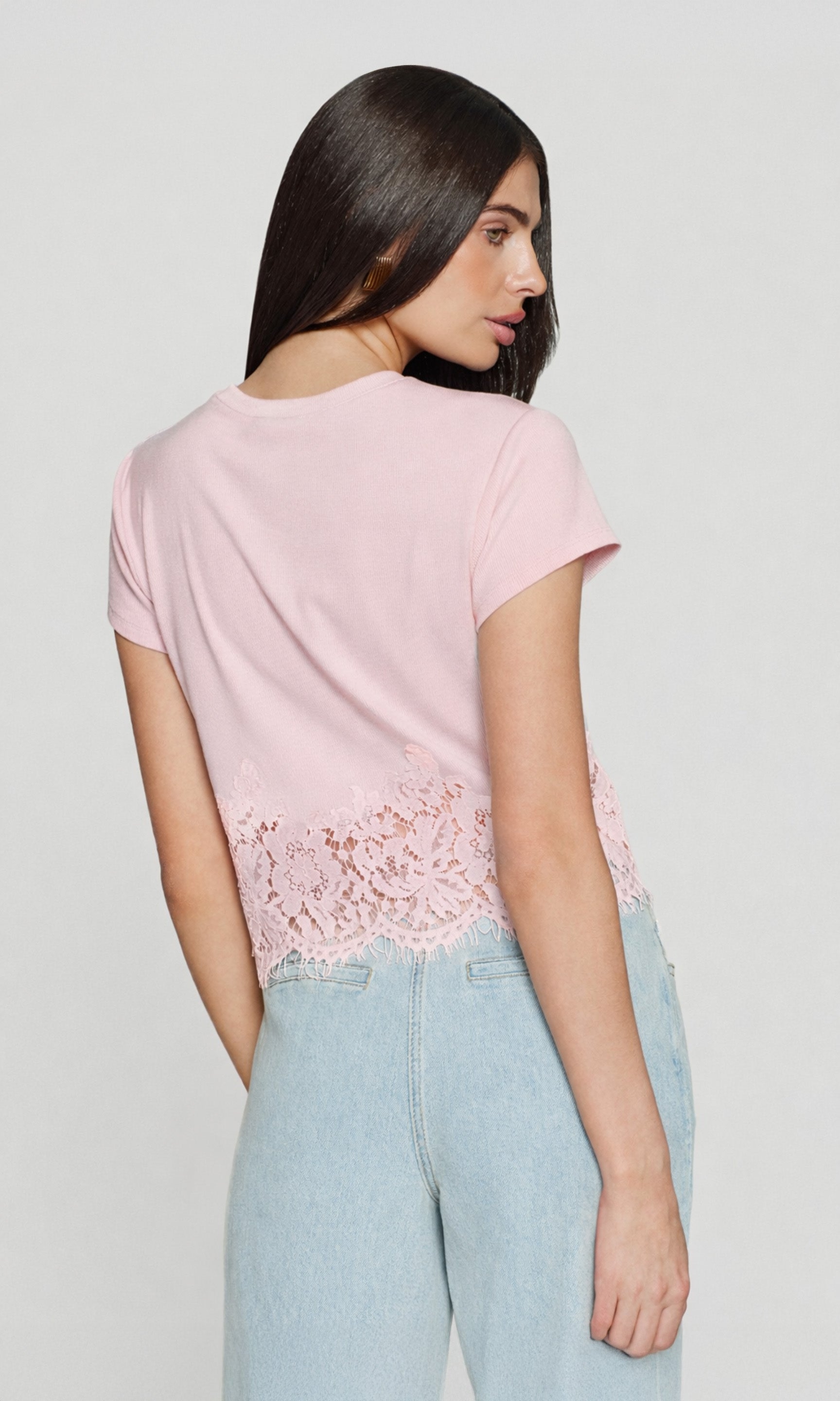 Back view of model wearing a pink top with a lace detailed hem with blue jeans