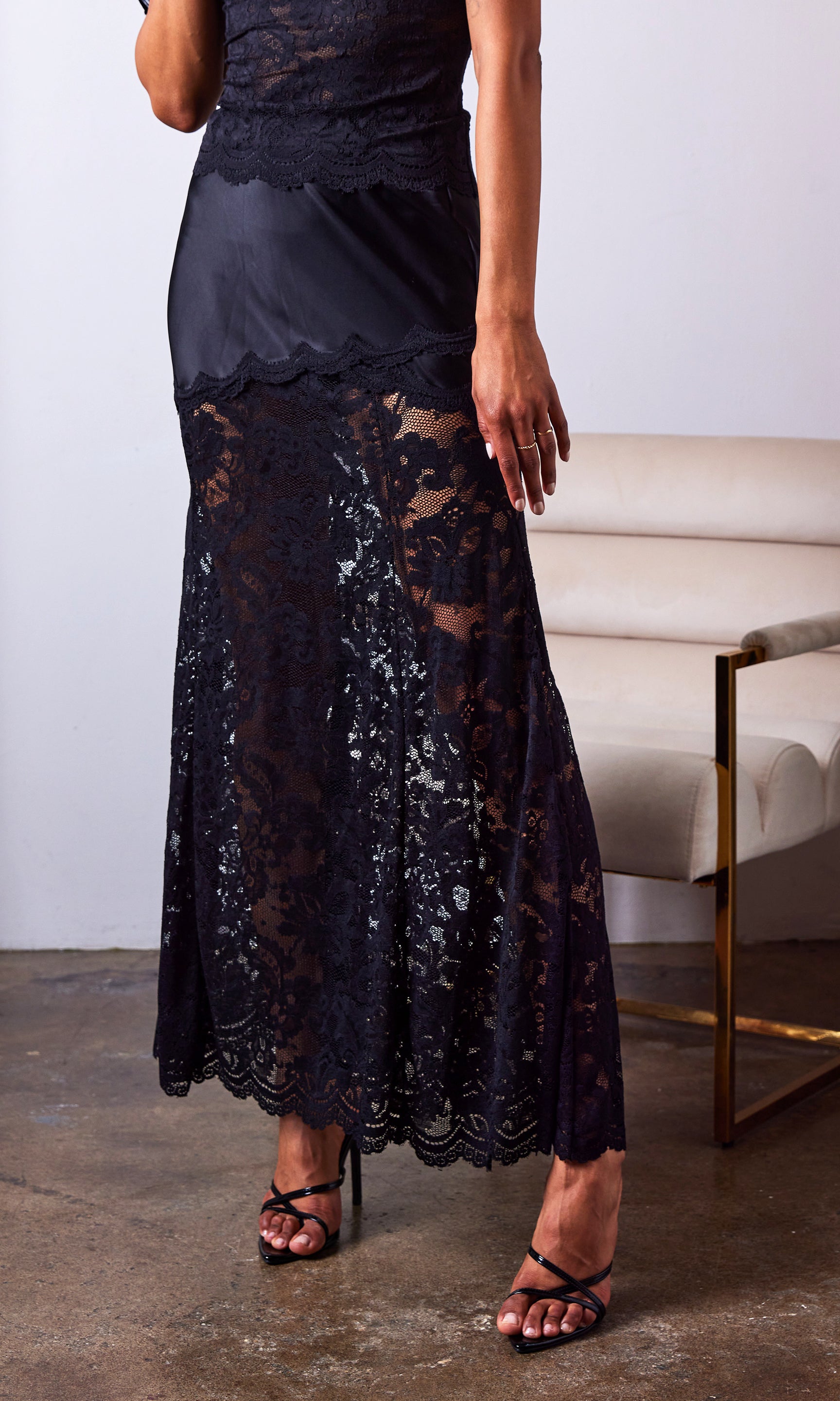 woman wearing a black lace skirt with a satin lining and paired with a black cami in front of a white chair
