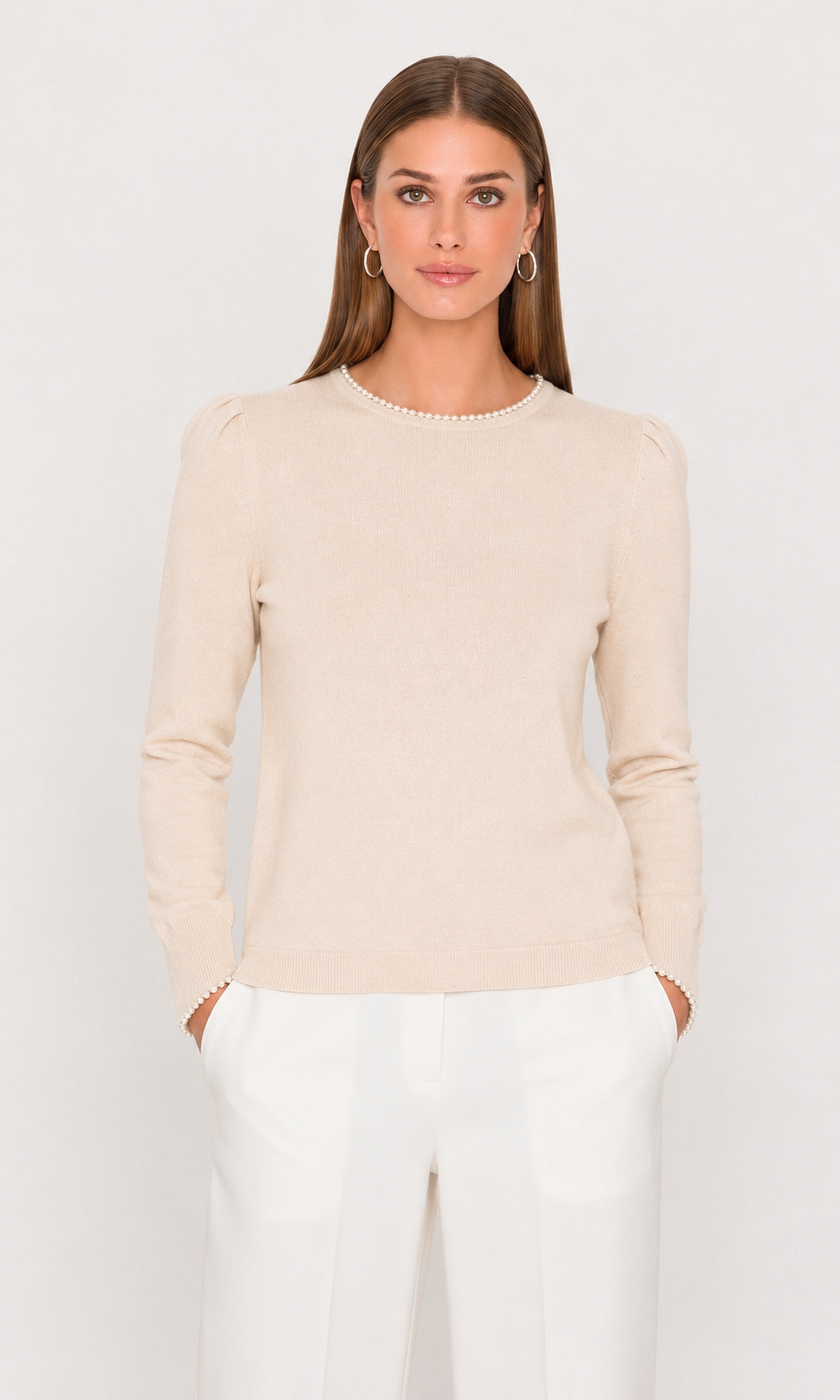 Woman wearing a beige long-sleeve top and white pants on a light gray background
