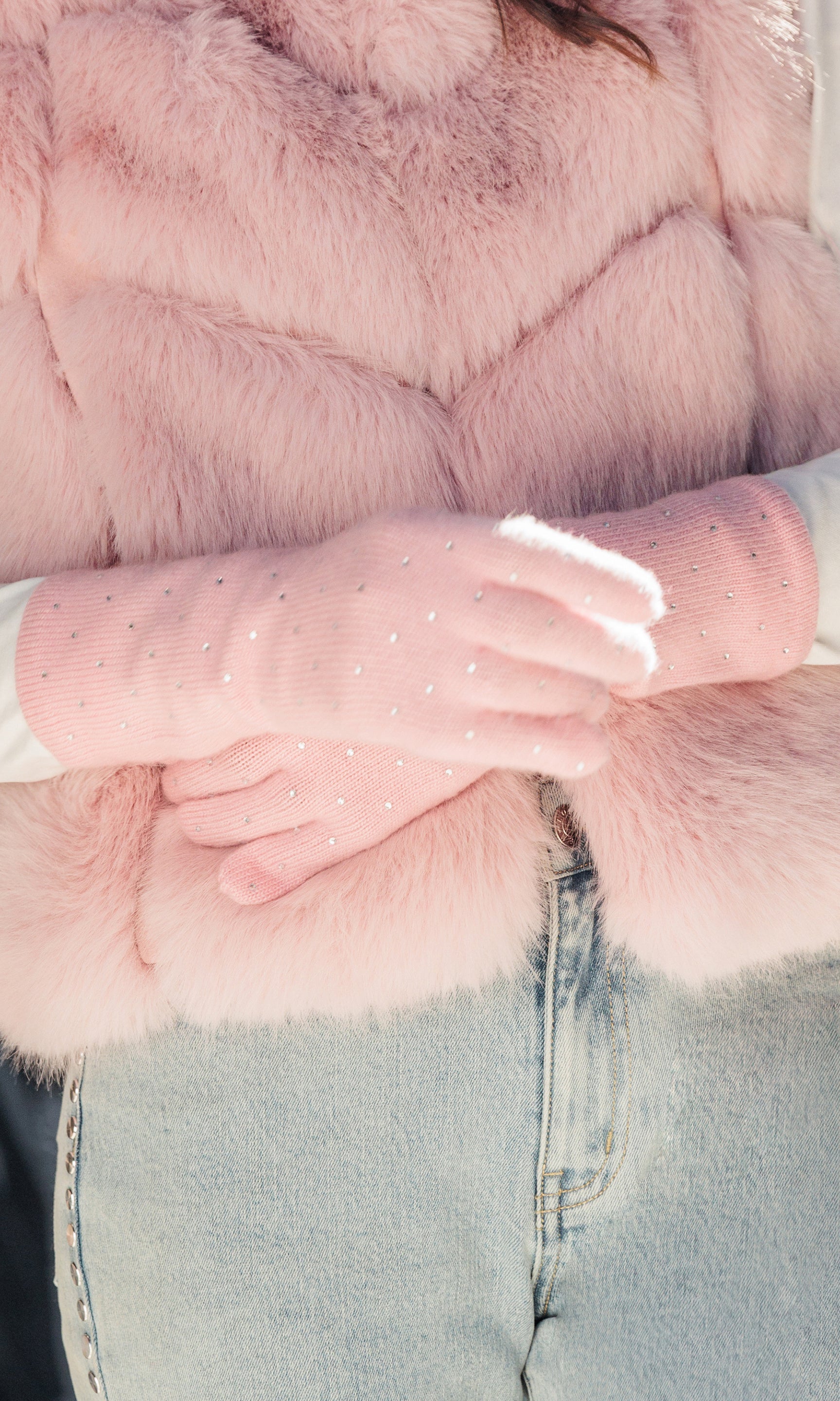 Close-up of a pink fur coat with a person wearing light blue jeans and white gloves.