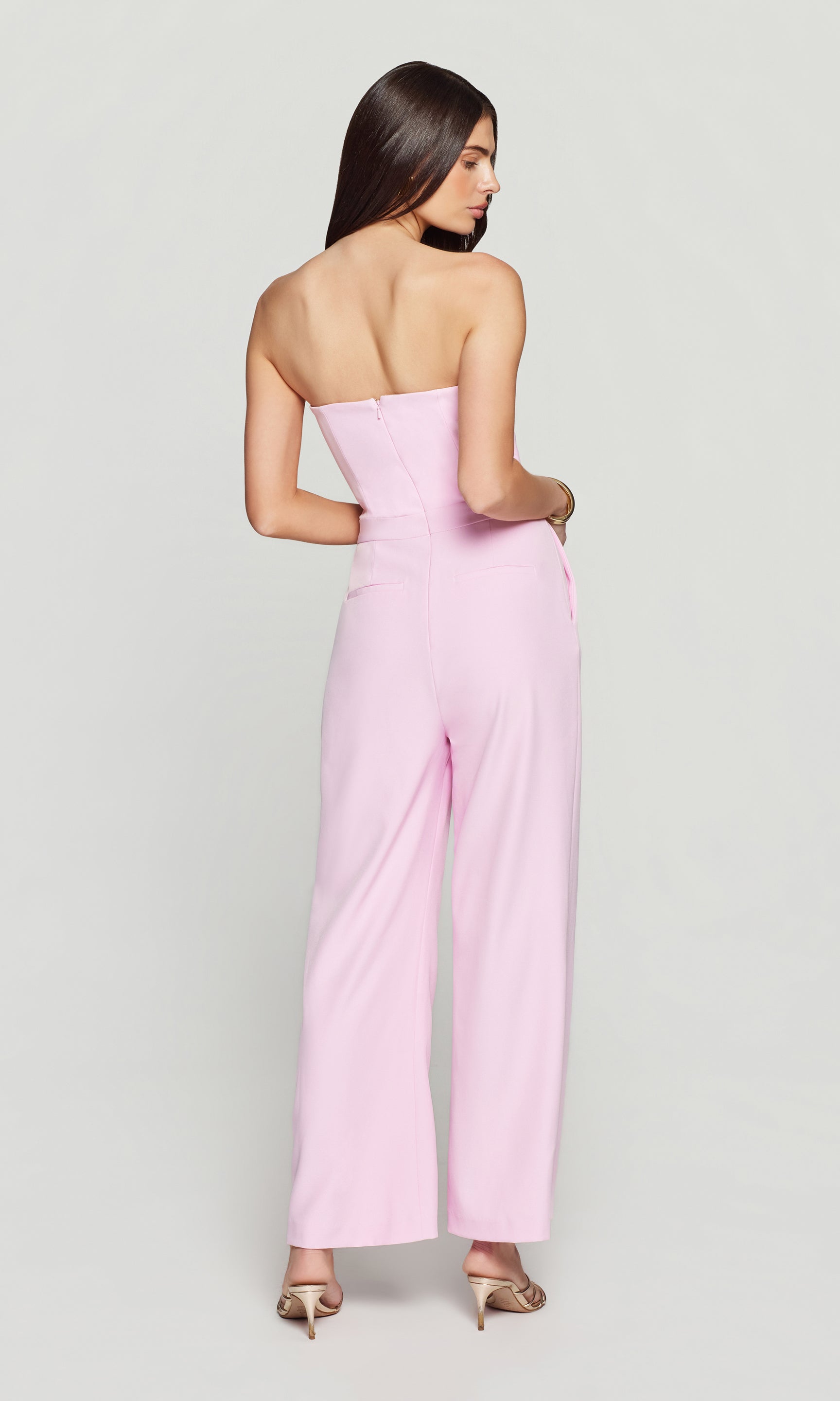 Back view of woman wearing a strapless pink jumpsuit on a white background