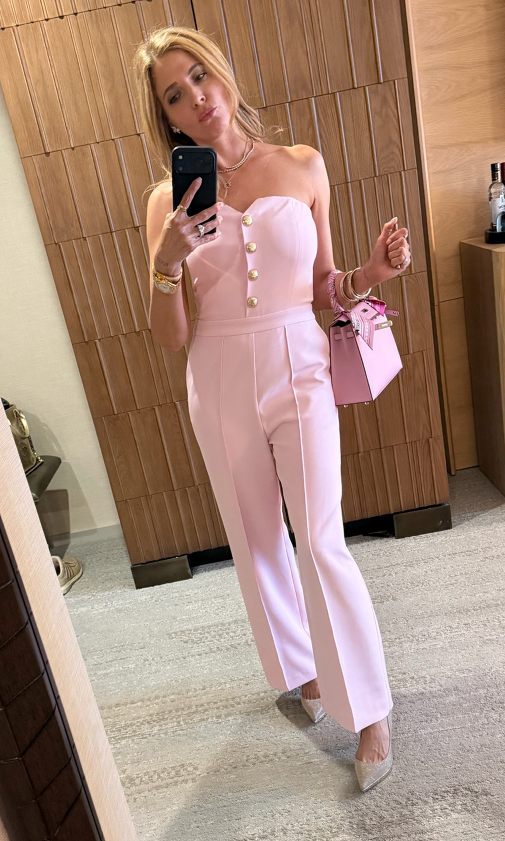 Founder Roni in a pink strapless jumpsuit taking a mirror selfie.