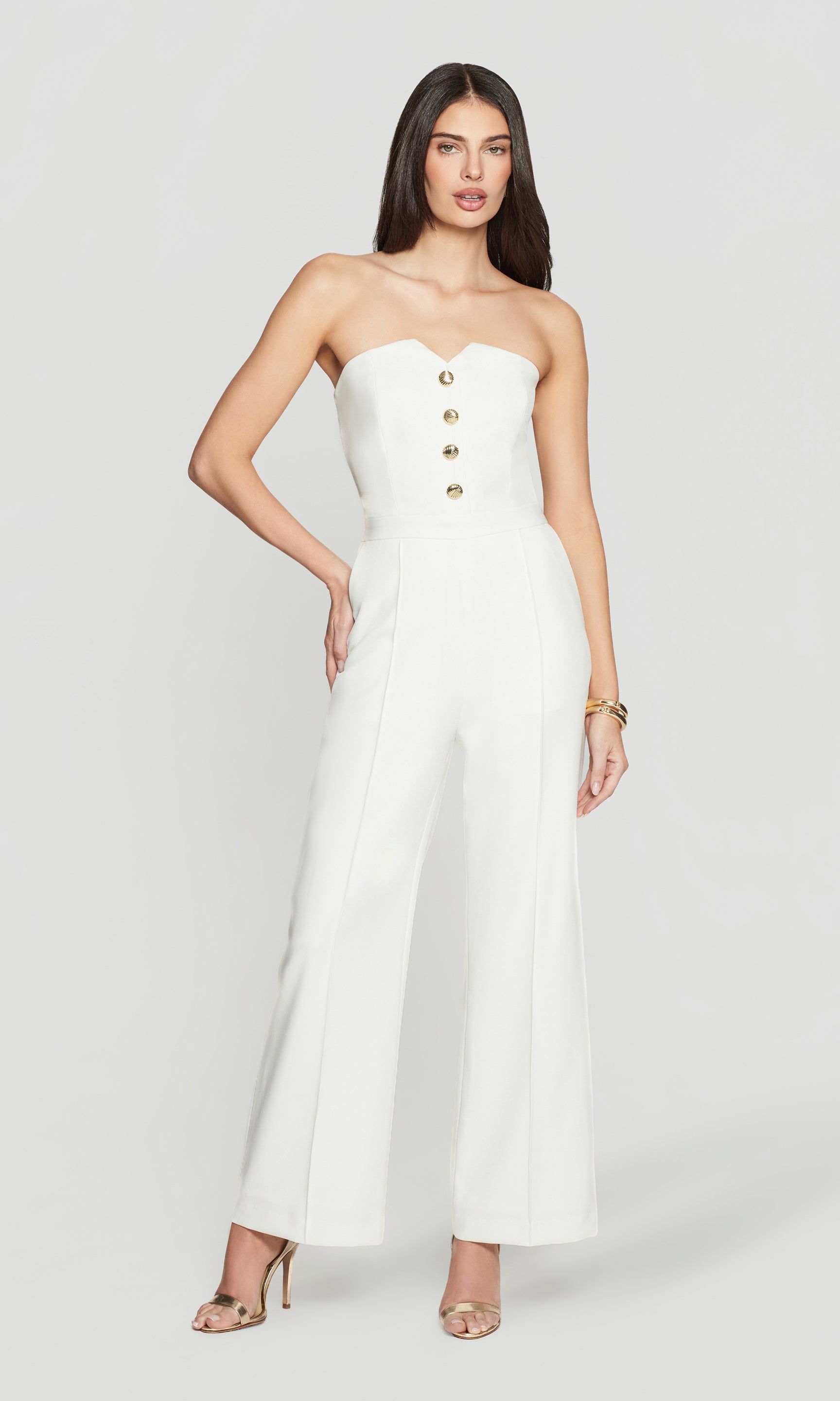 Woman wearing a white strapless jumpsuit with gold buttons on a white background