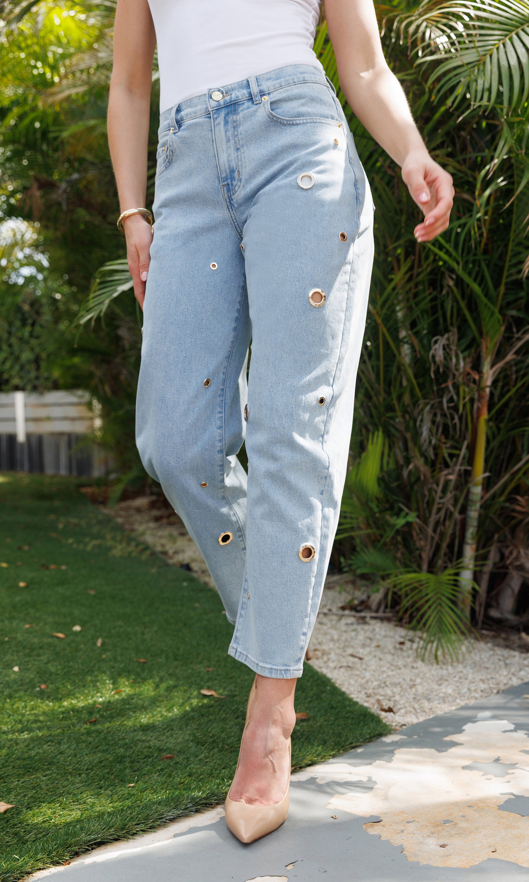 Person wearing light blue jeans with decorative grommets outdoors.