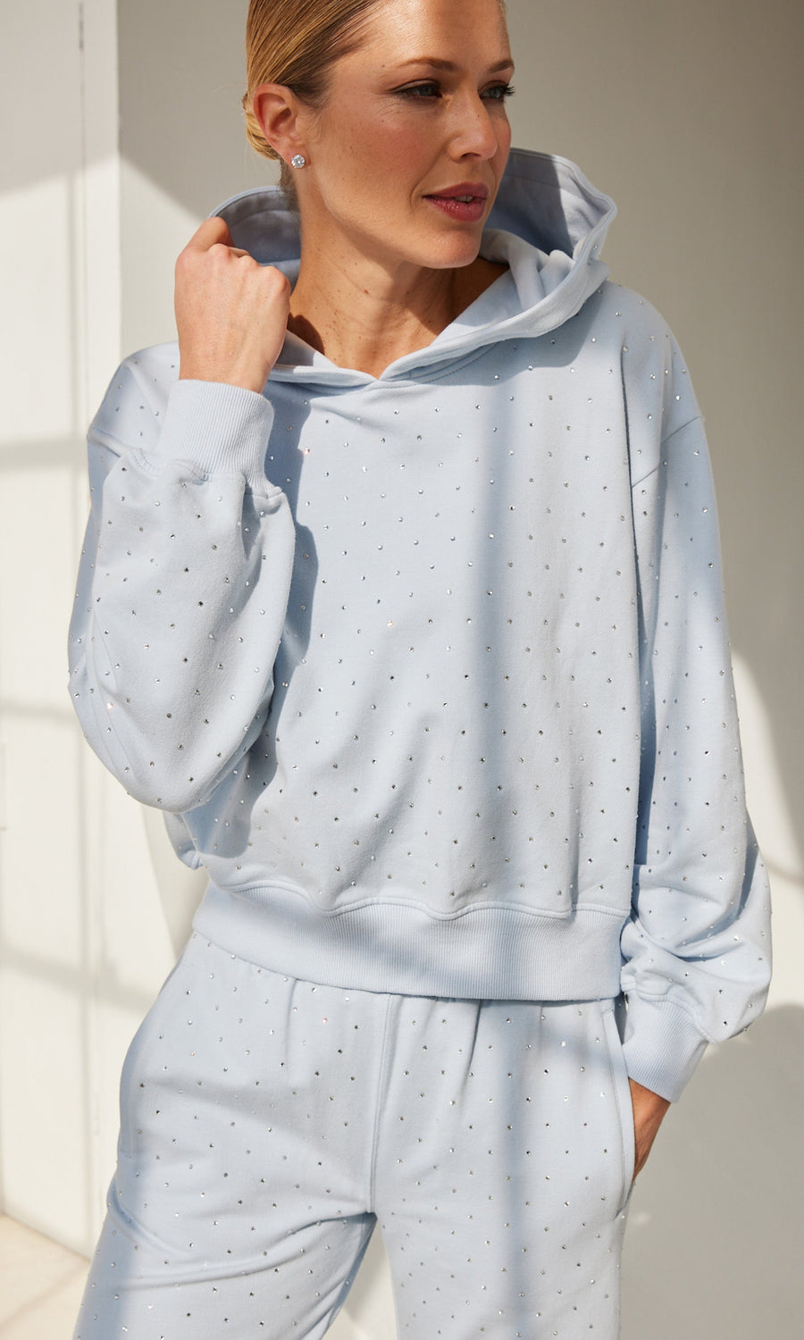 The model poses casually in a light blue hoodie and sweatpants, exuding a laid-back vibe.