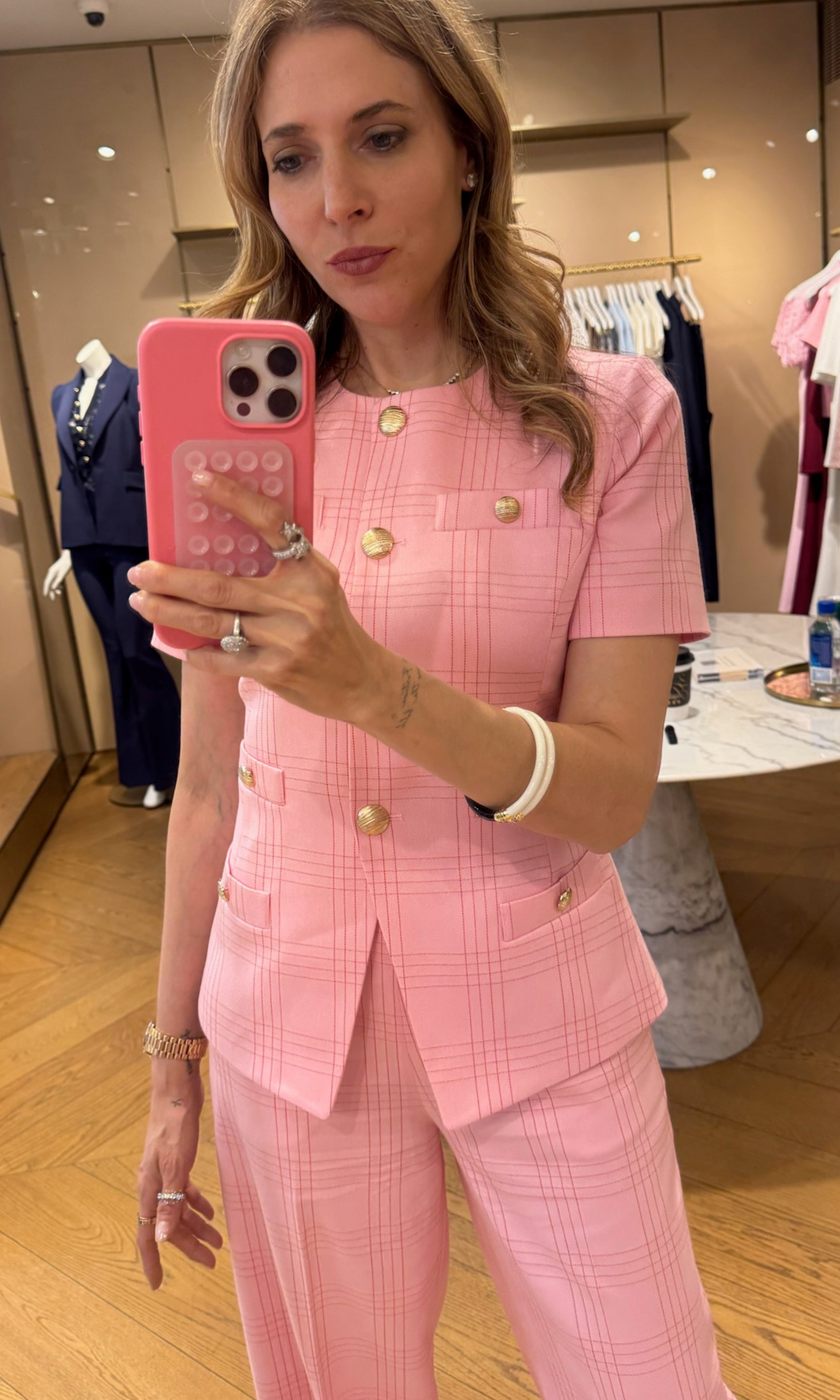 Woman in a pink checkered suit taking a mirror selfie in a store.