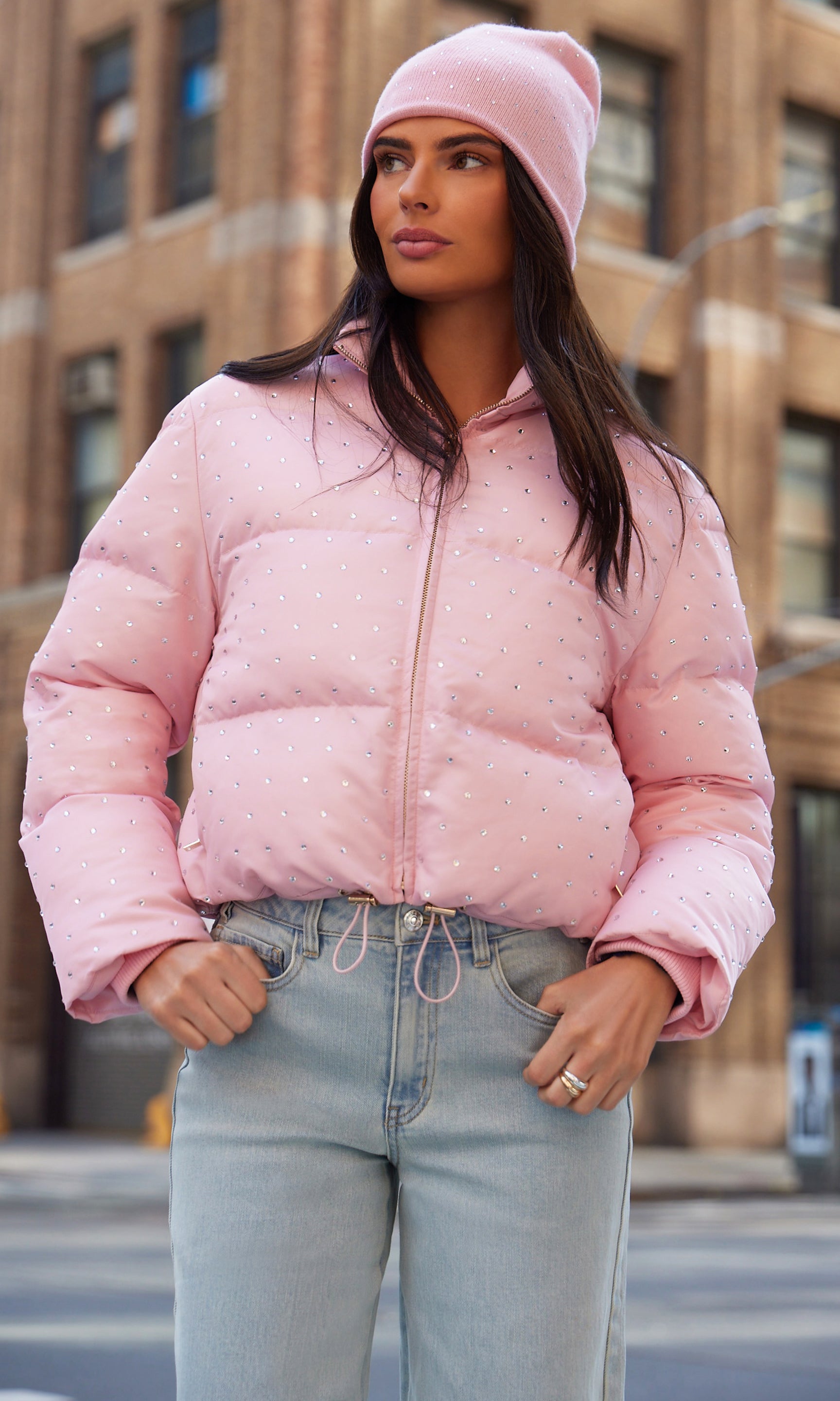 Woman wearing a pink puffer jacket and beanie in an urban setting