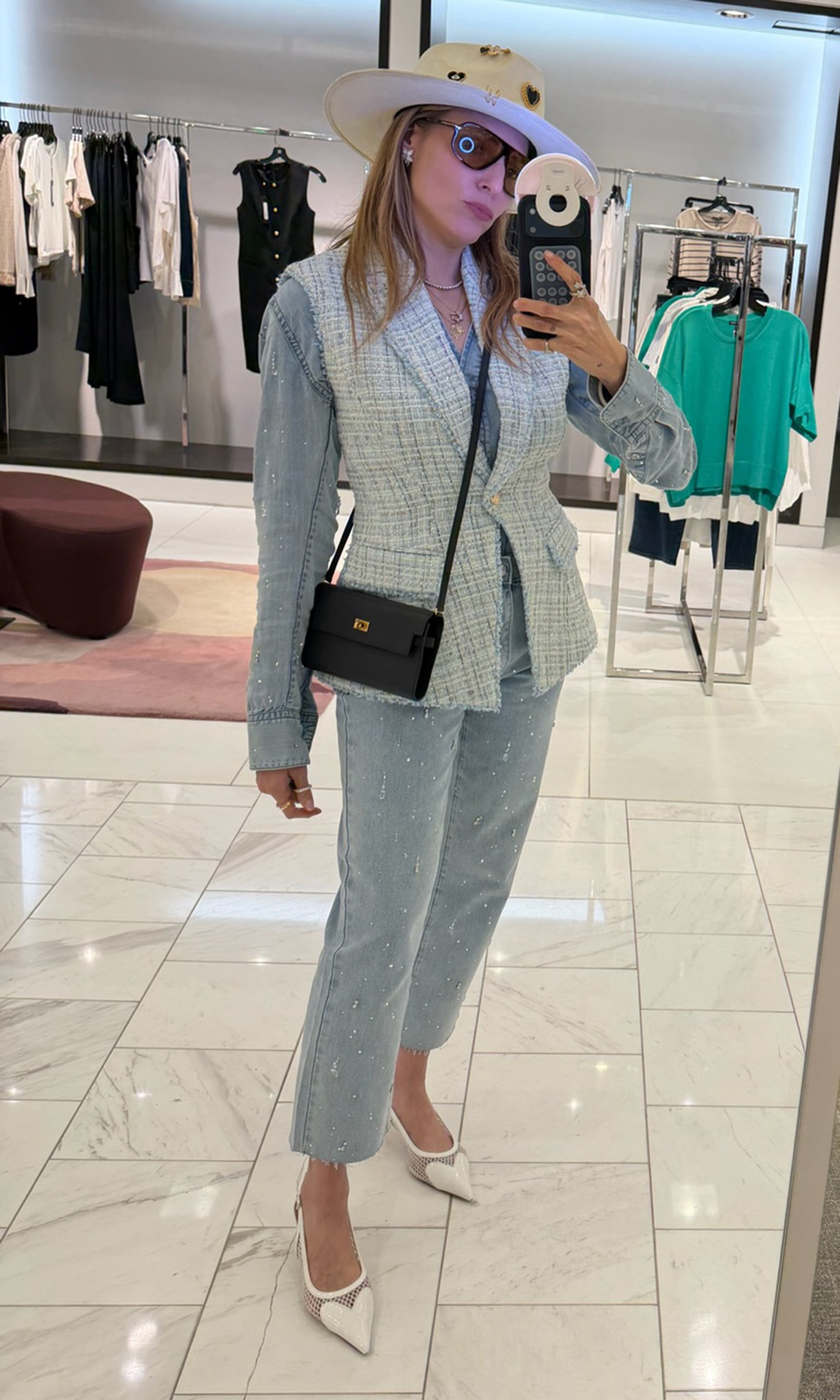 Founder Roni taking a mirror selfie in a store, wearing a checkered blazer and pants with a black handbag.