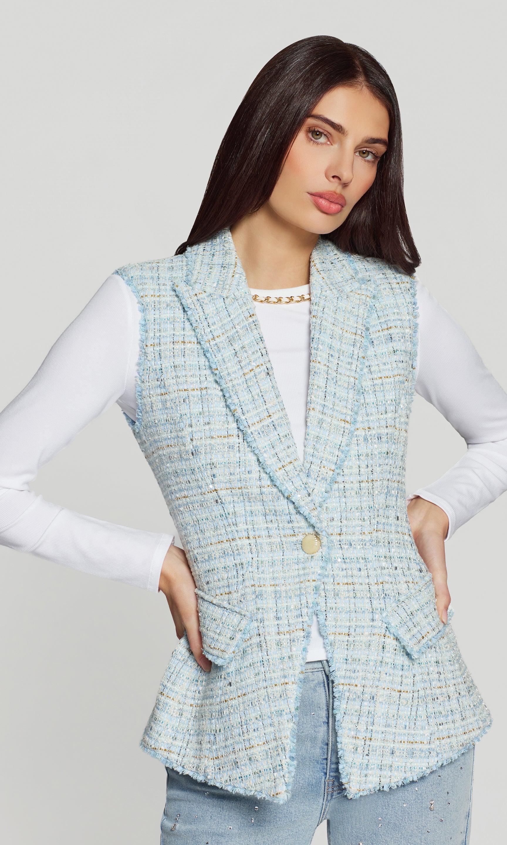 Woman wearing a light blue tweed blazer over a white shirt on a plain background