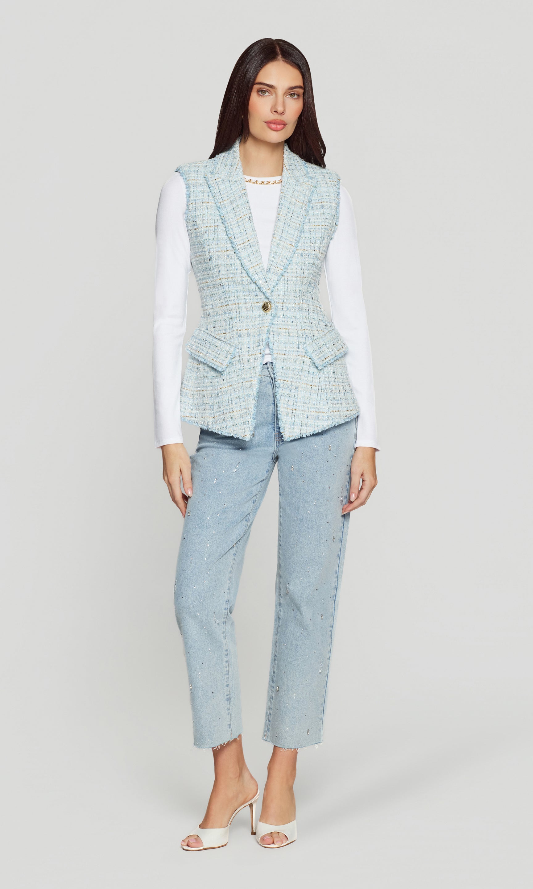 Woman wearing a light blue tweed vest over a white shirt with light blue jeans on a white background
