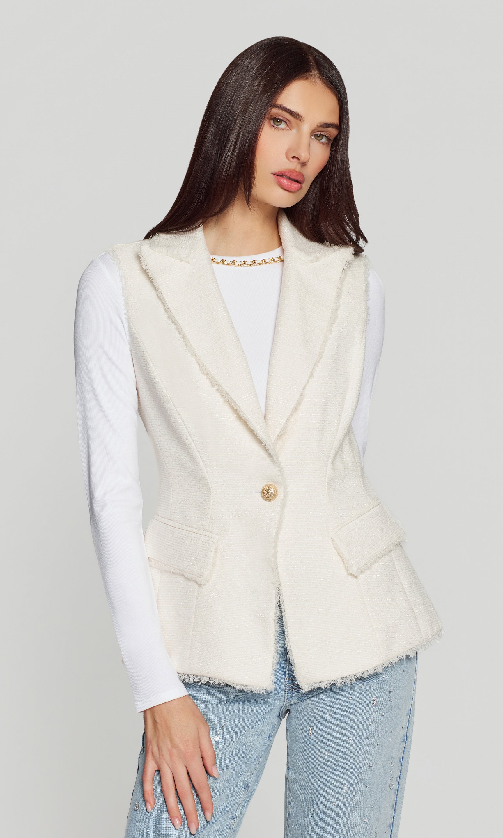 Woman wearing a white vest over a white shirt with a plain background