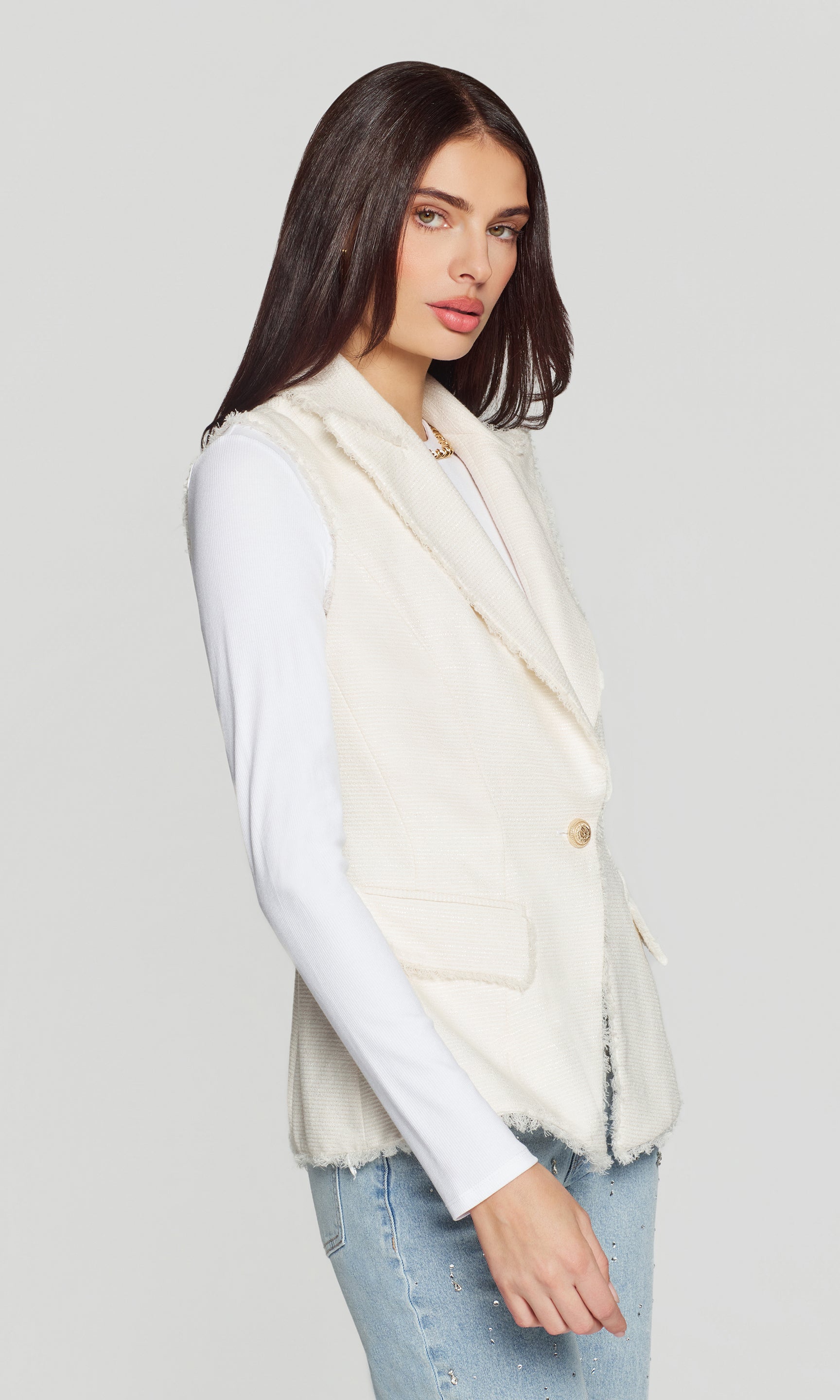 Woman wearing a cream-colored vest over a white shirt on a light gray background