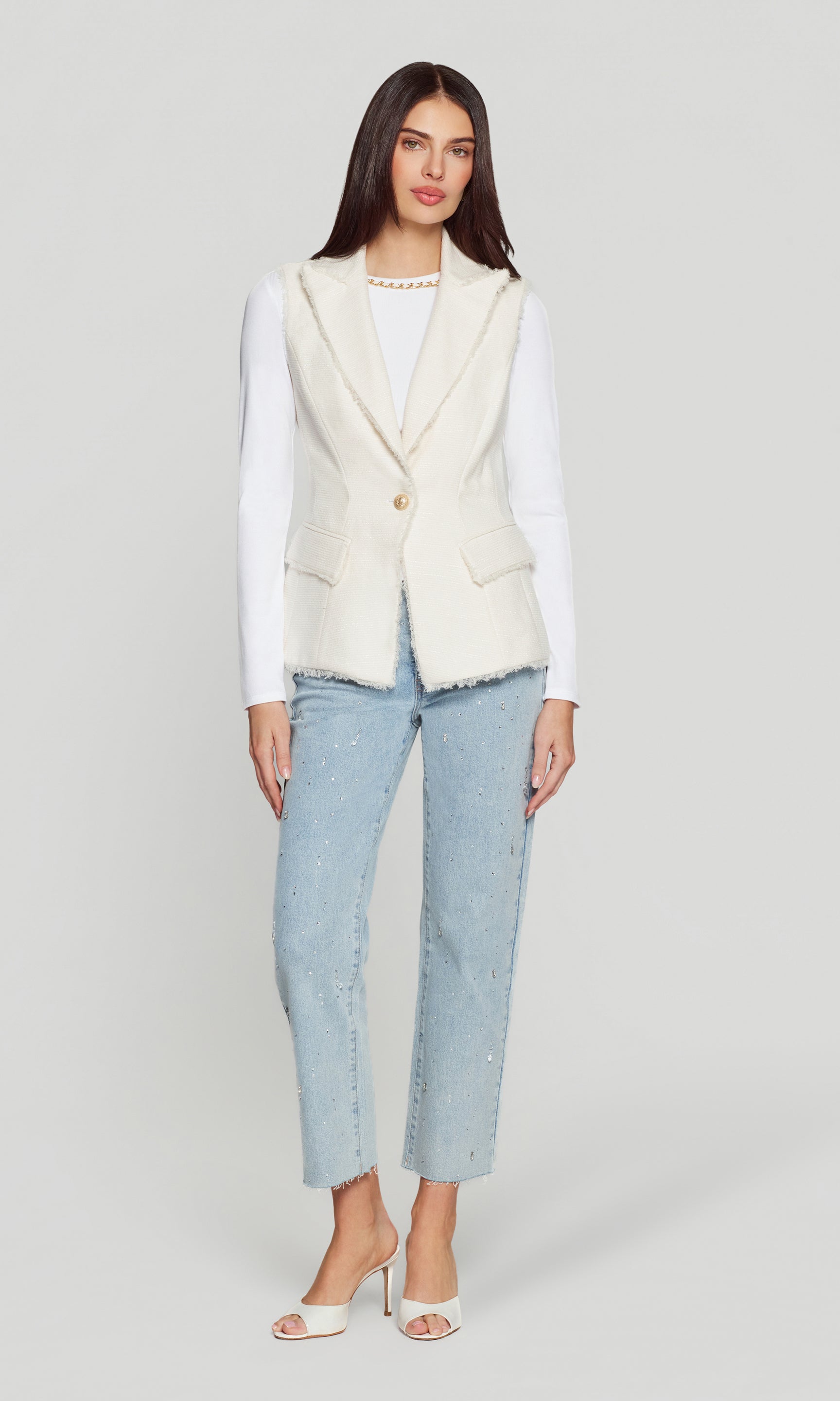 Woman wearing a cream vest over a white shirt with light blue jeans on a white background