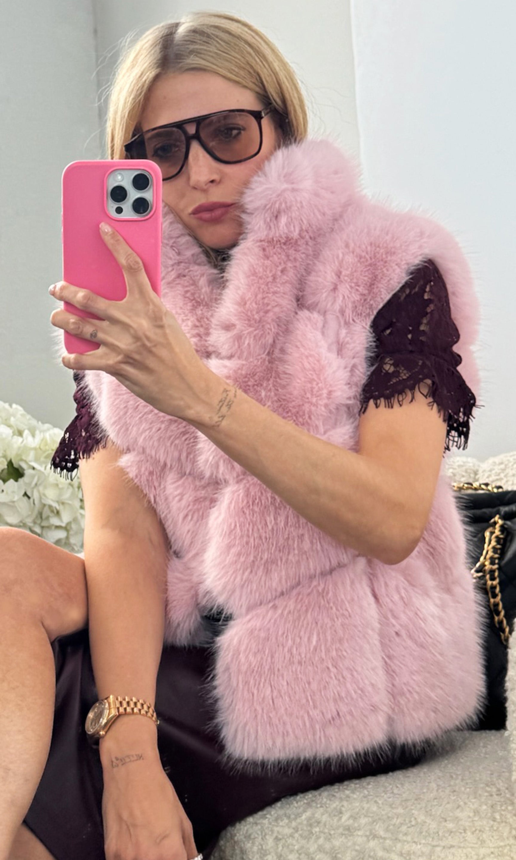 Our founder Roni wearing a pink faux fur vest with black lace top, sitting on a couch.