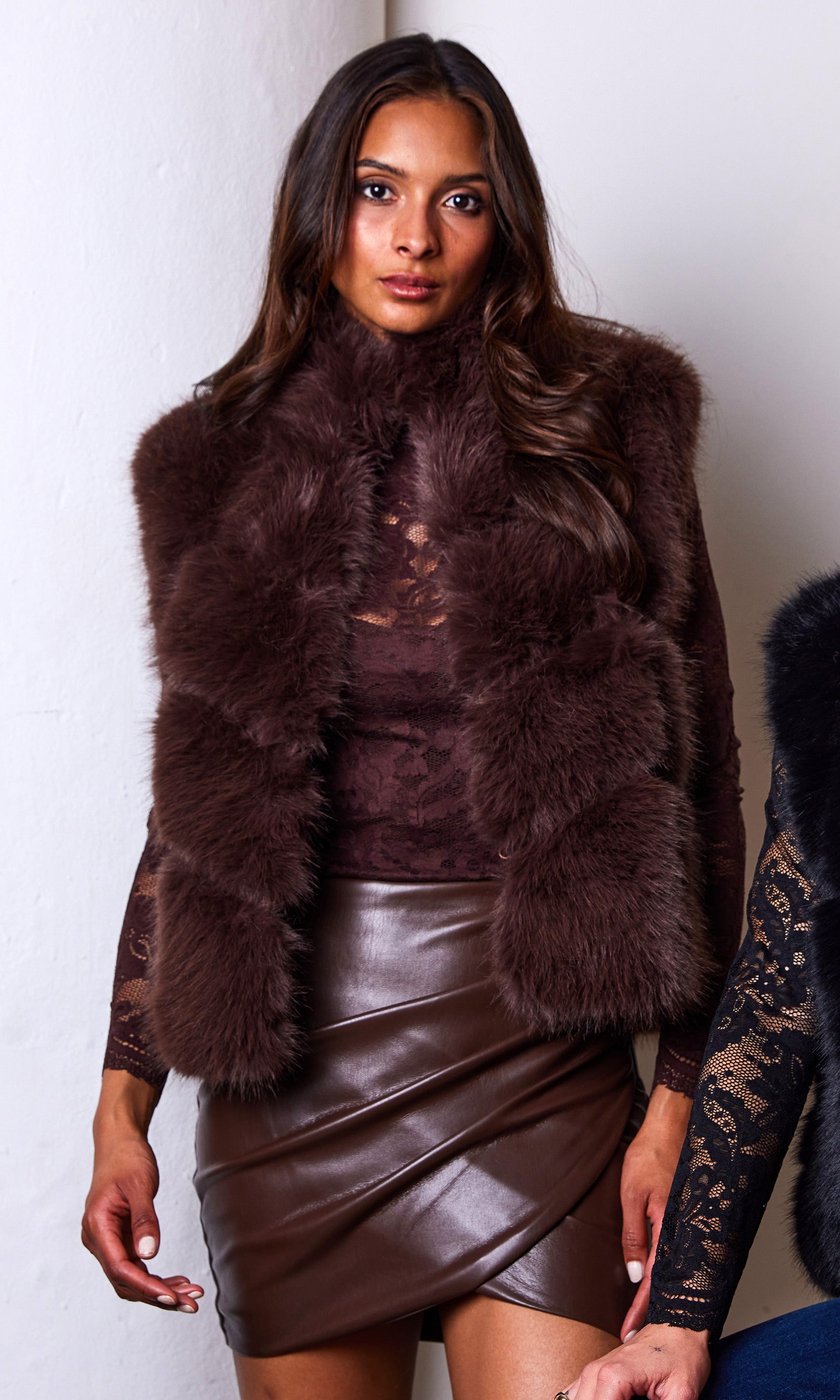 Woman wearing a brown fur vest and leather skirt against a white background