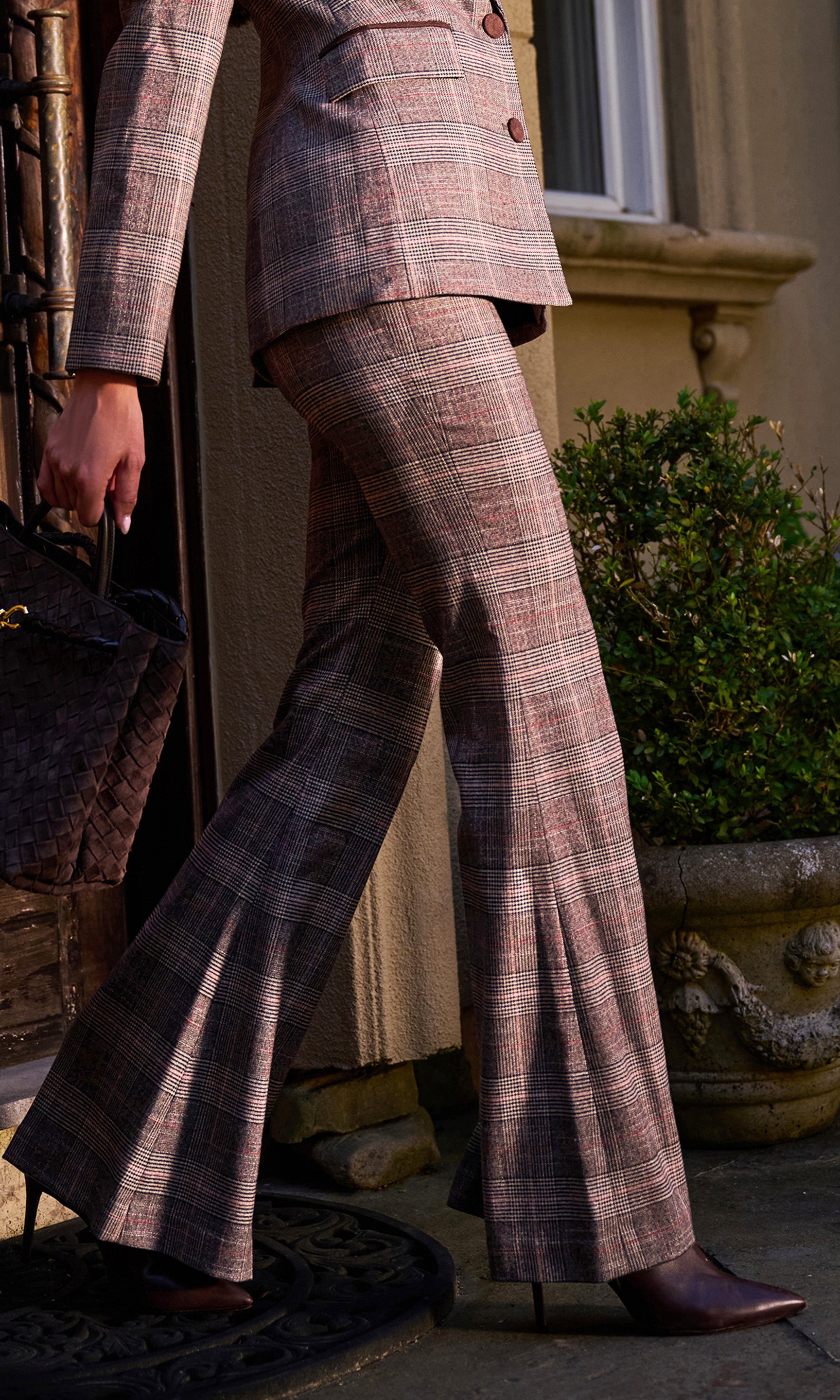 A person wearing a tailored plaid suit with a cropped blazer and matching wide-leg flared trousers, standing outdoors near a building.