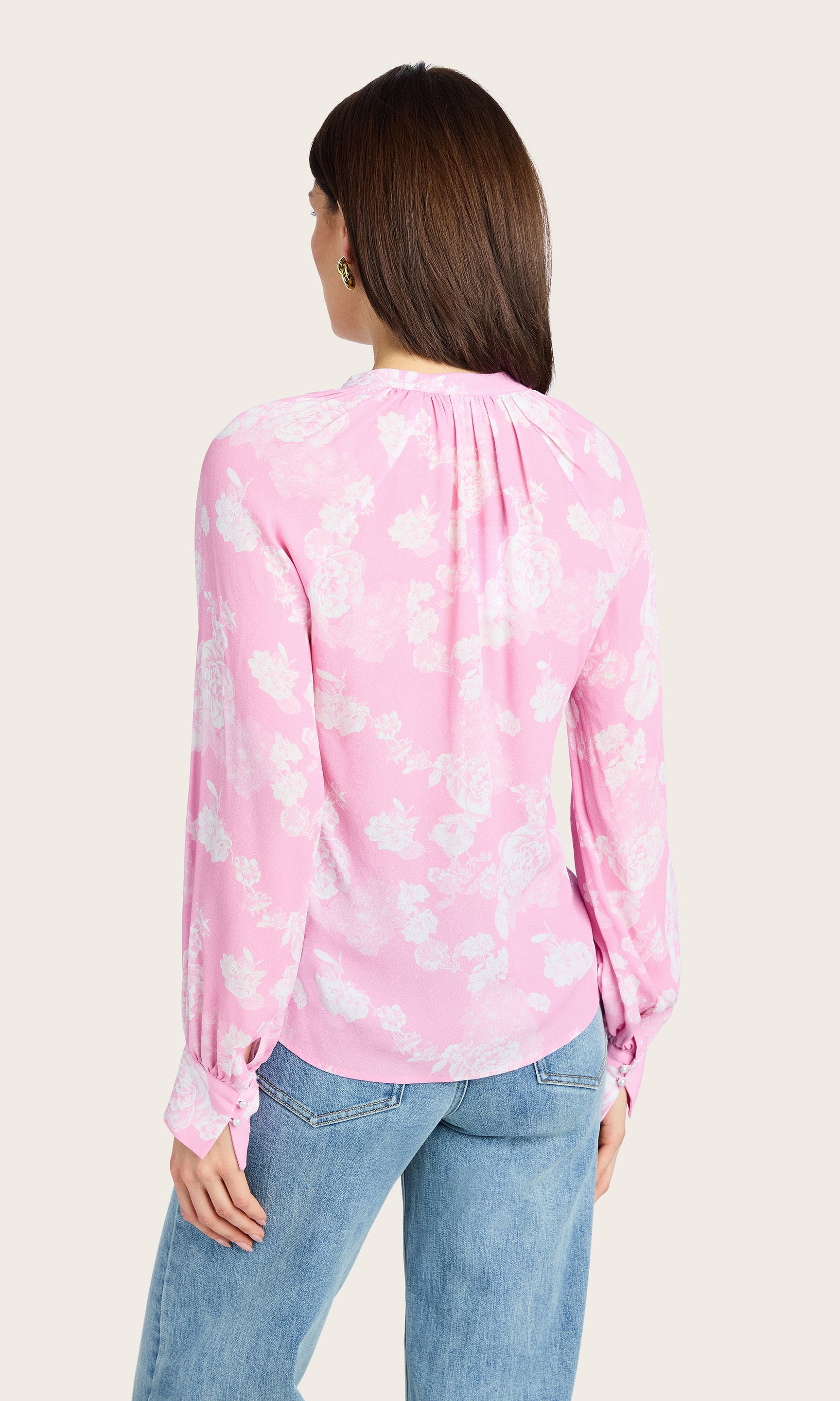Rear view of the model showing the pink and white floral pattern and loose fit of the Sophia Floral Blouse, paired with blue jeans.