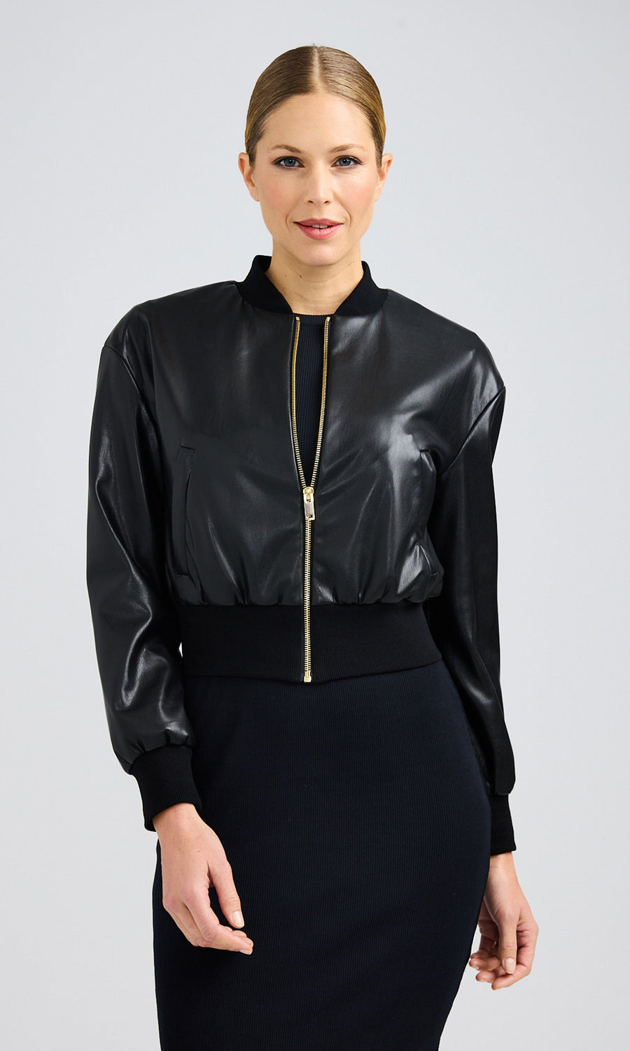 Model wearing black vegan leather jacket zipped half way with gold zipper.