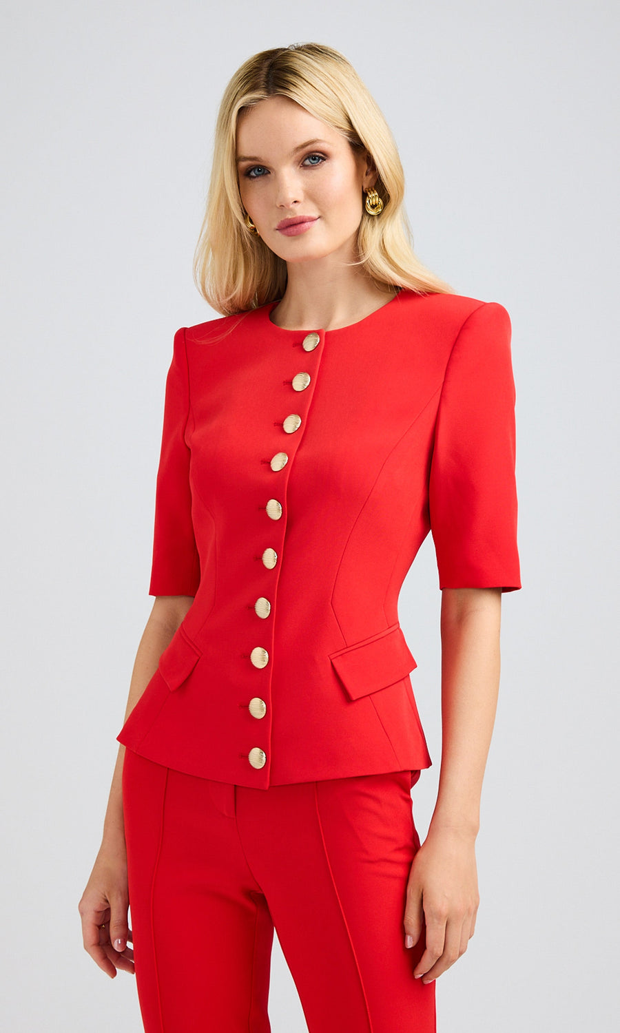 Side view of a blonde model in a red lightweight crepe jacket with short sleeves and gold buttons.