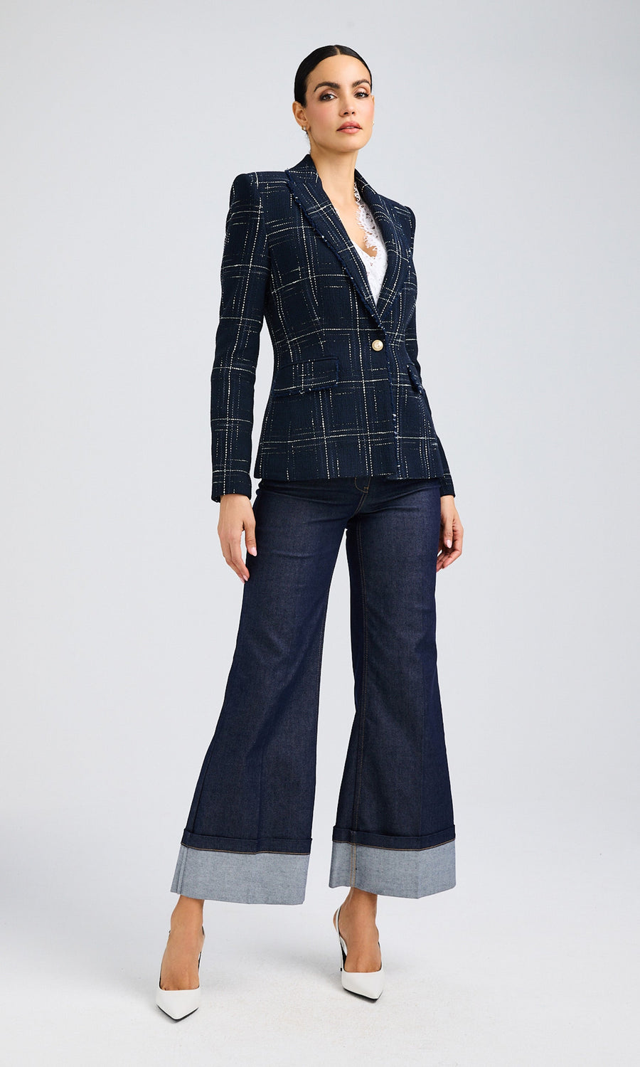 Woman wearing a navy tweed blazer over a white camisole paired with wide-leg jeans and white heels.