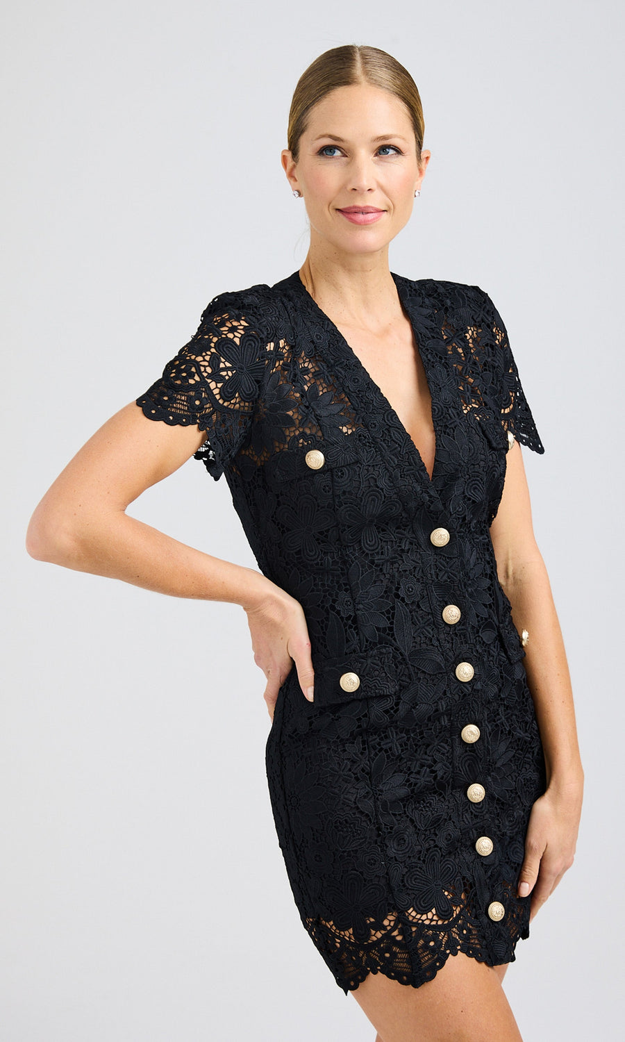 Front view of the model wearing a black lace dress with gold button details, styled with a sleek updo.