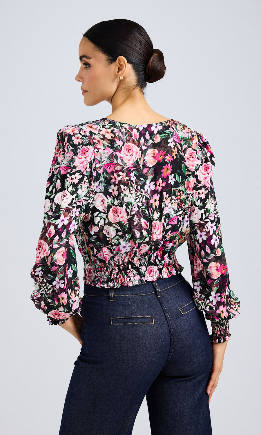 Back view of model wearing a vibrant floral wrap blouse with long sleeves and dark denim jeans.