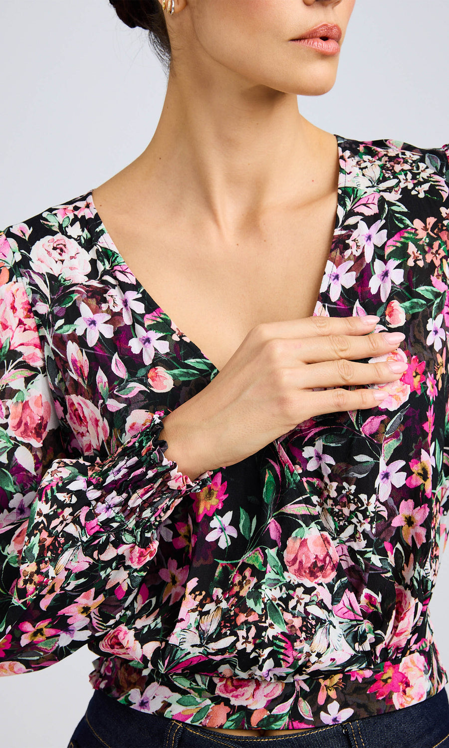 Close-up of the floral wrap blouse, focusing on the vibrant floral print and gathered sleeve detail, with the model's hand lightly resting near the neckline.