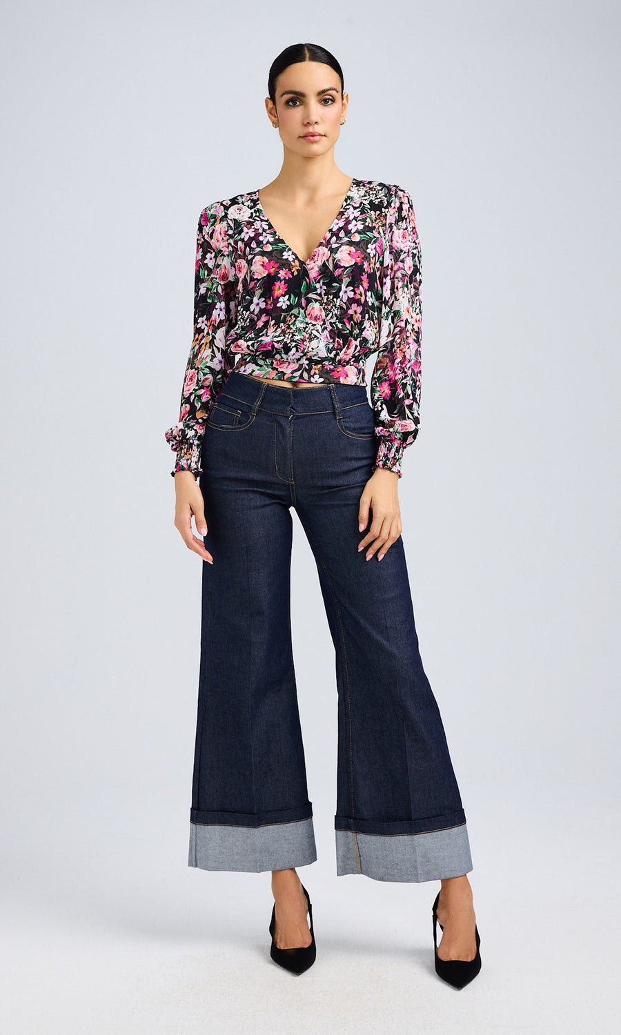 Full-body shot of the model in a floral wrap blouse paired with flared dark denim jeans and black heels, emphasizing the flowy blouse and structured jeans.