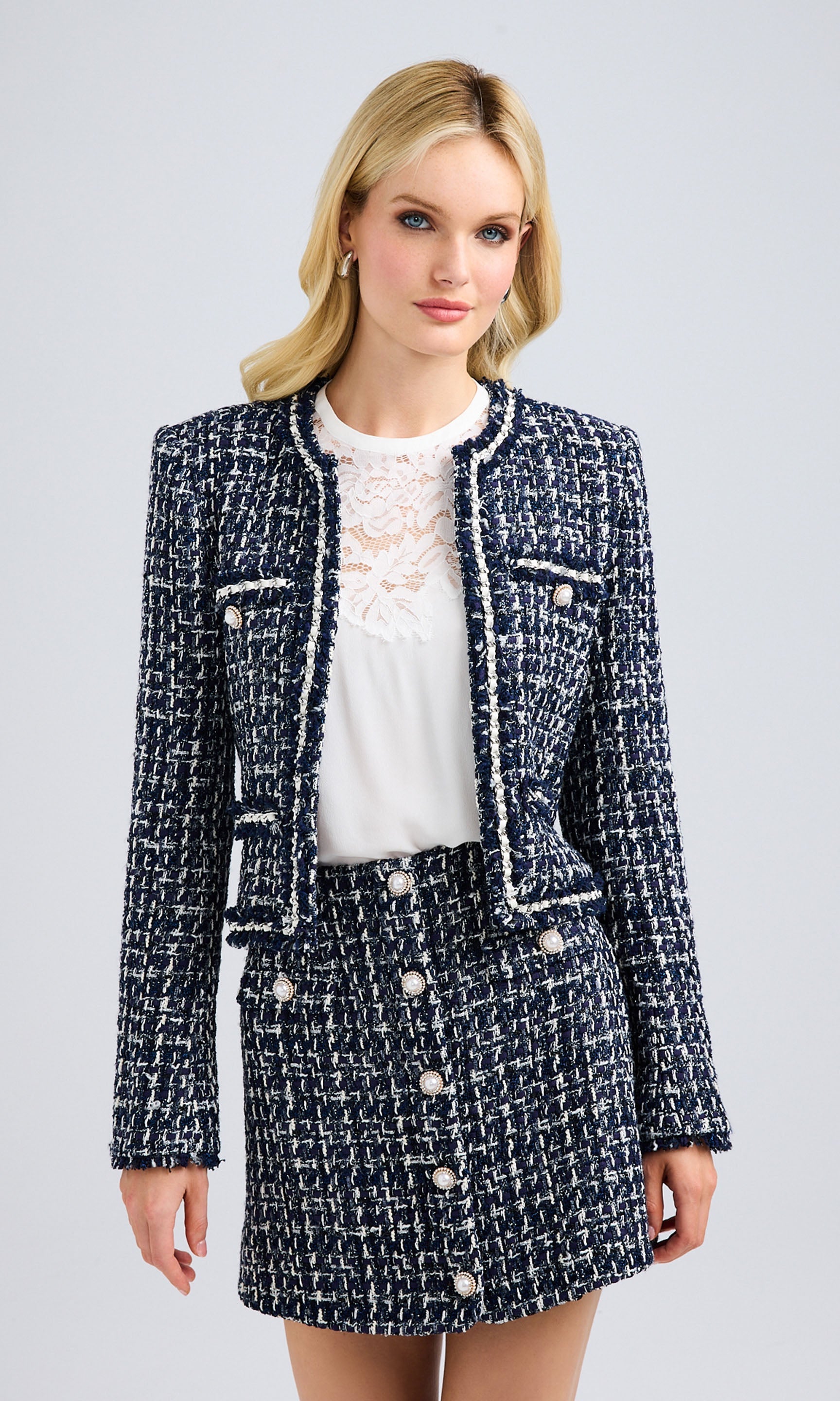 Front view of a navy and white tweed blazer styled with a matching tweed skirt, showcasing intricate texture and pearl buttons