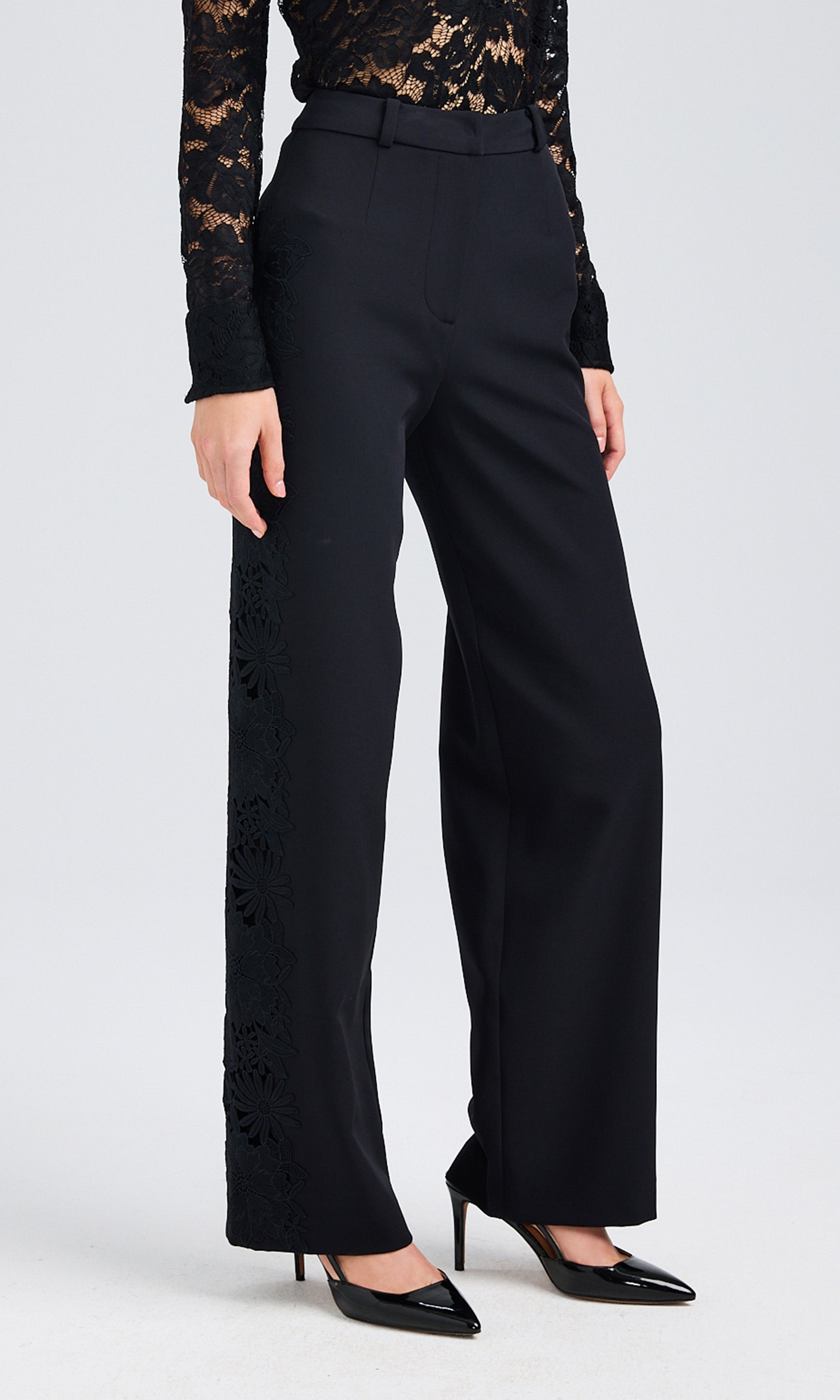 Close-up of woman wearing black slacks with lace details paired with black heels and a lace shirt.